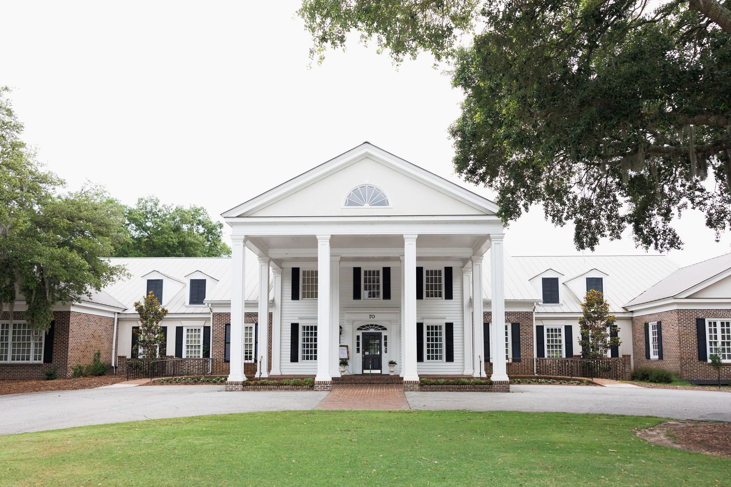 Grand white colonial wedding venue with large columns, brick wings, and manicured lawn on overcast day.