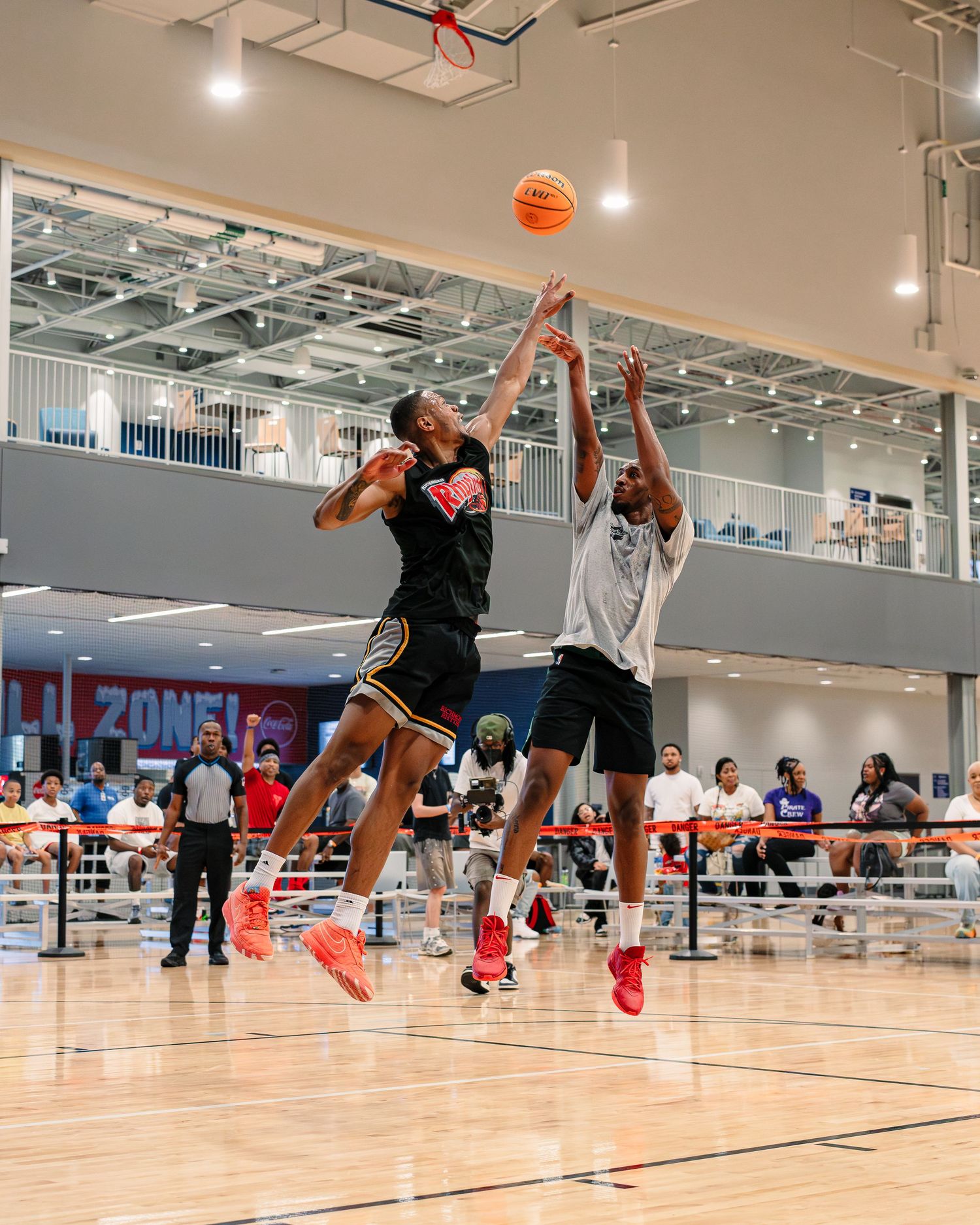 Two basketball players jump high to compete for a rebound during an indoor game.