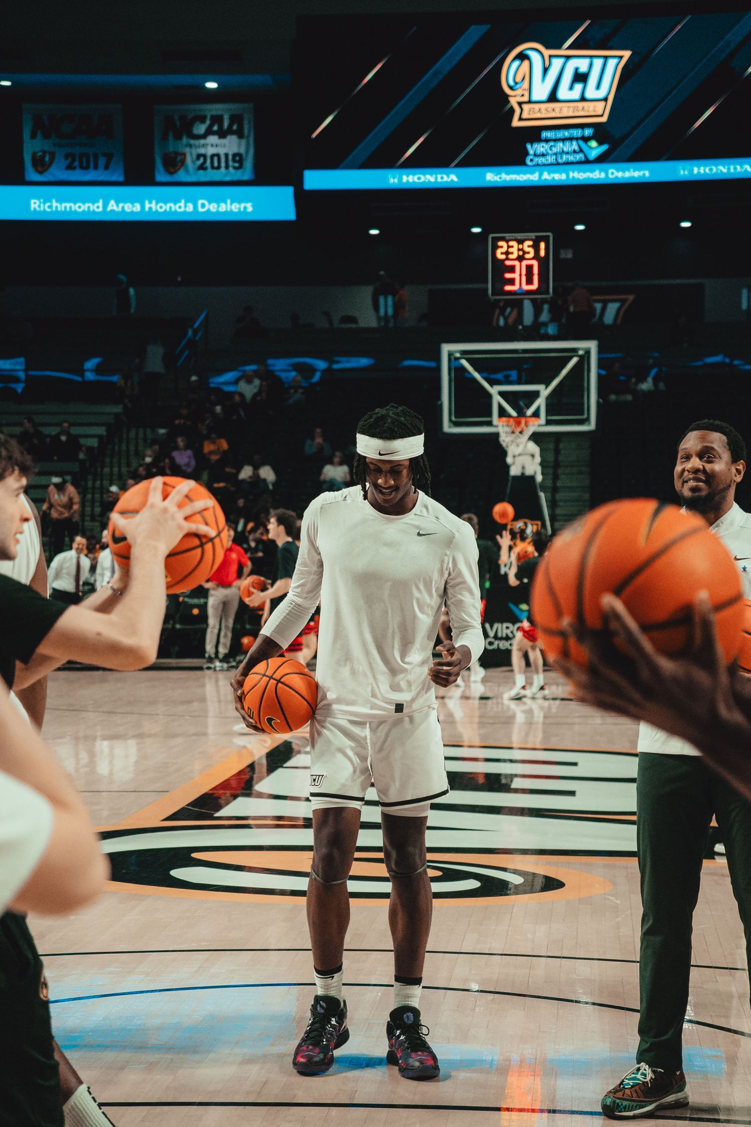 Basketball players practice shooting drills on a VCU court with multiple basketballs in play.