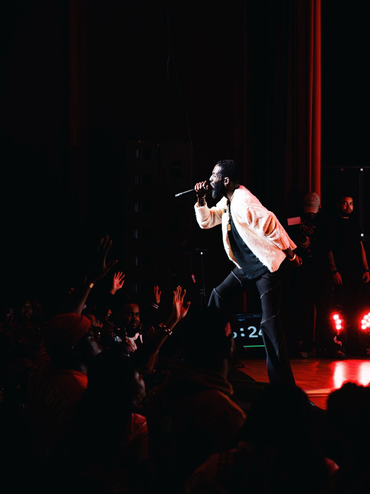 Concert performer on dark stage illuminated by red lights with crowd in foreground.
