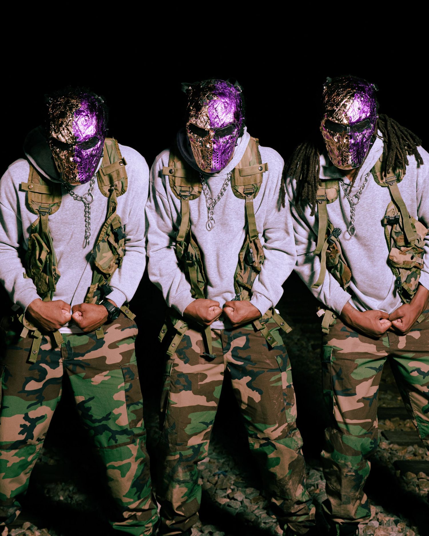 Three masked figures in camouflage pants and tactical gear pose against a dark background.