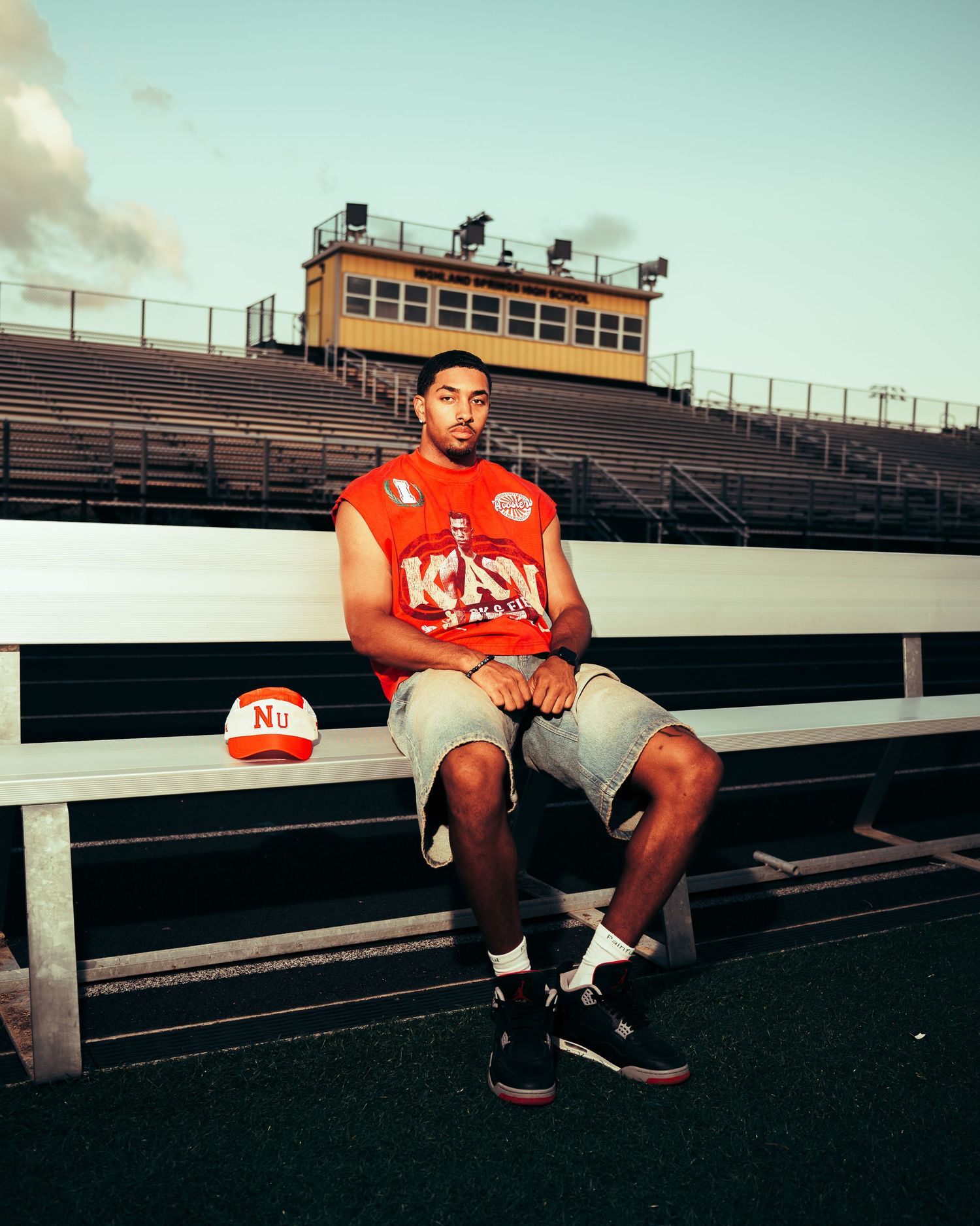 Athletic figure in red jersey sitting on stadium bleachers during golden hour.