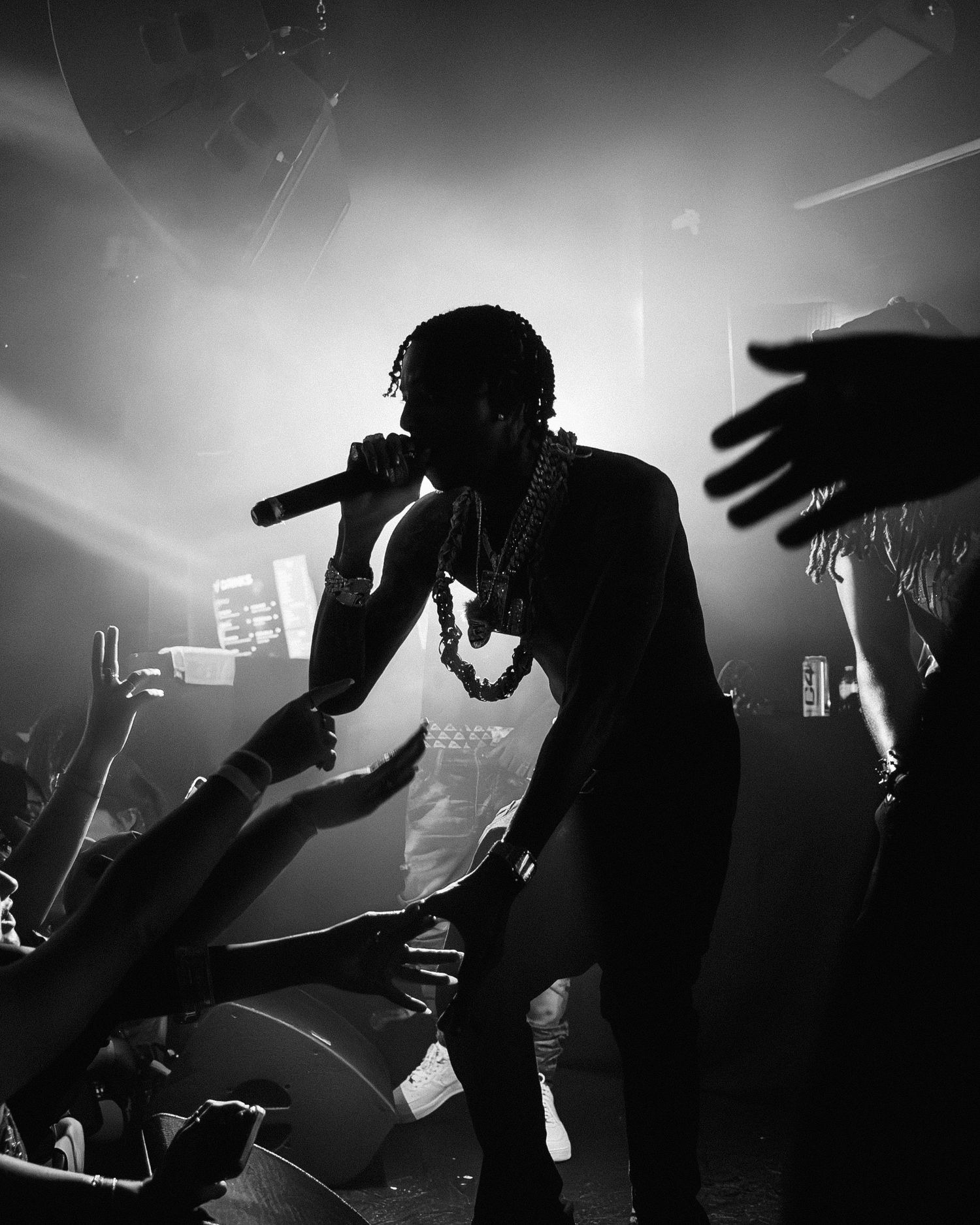 Black and white concert photography showing silhouettes of performers and audience hands in dramatic lighting.