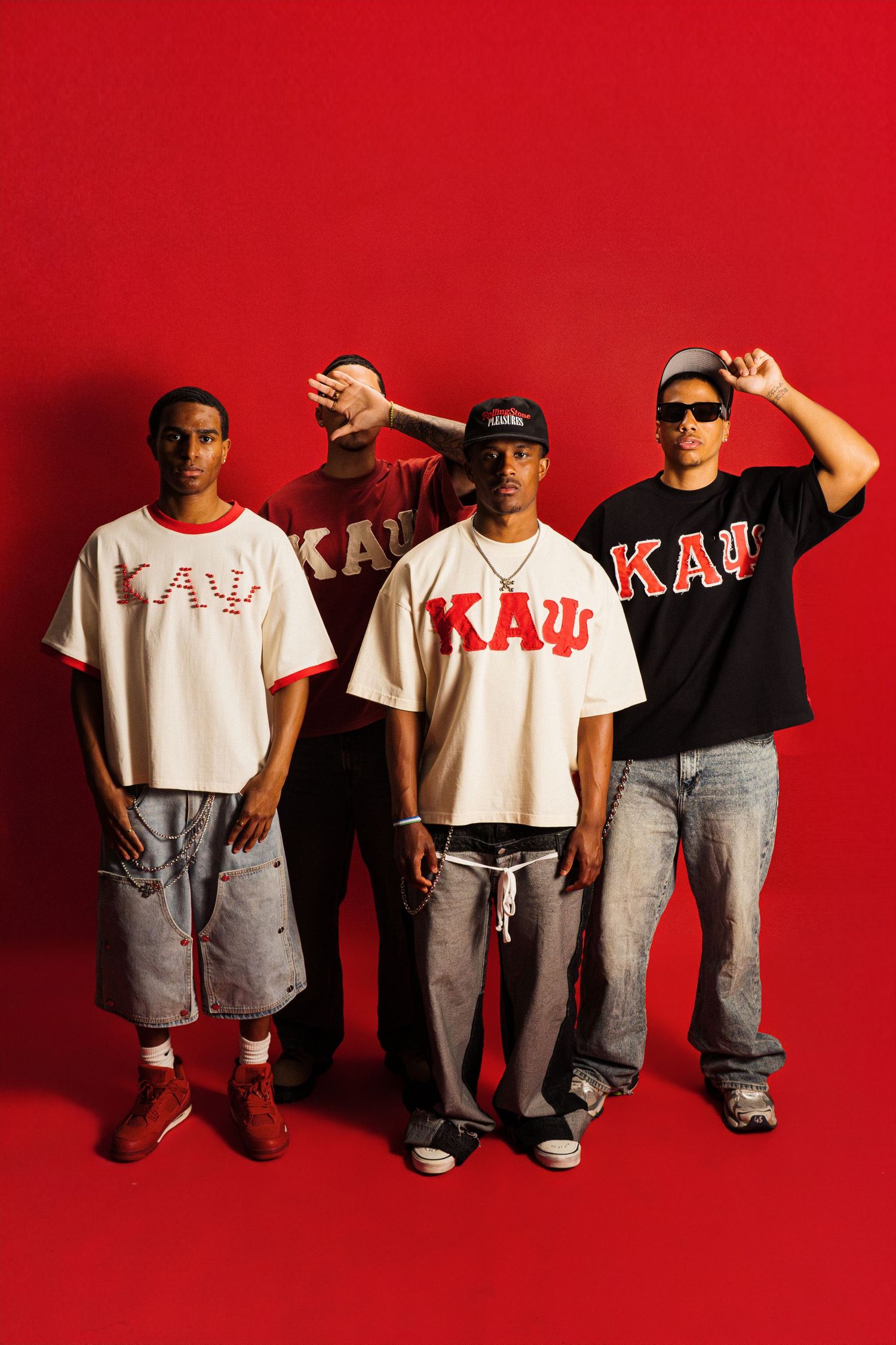 Four young men wearing KAΨ fraternity shirts pose confidently against a bold red background.