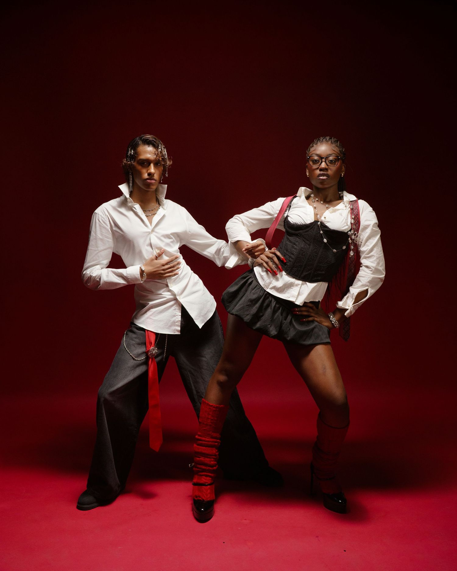 Fashion models in white tops and black bottoms pose dramatically on red background.