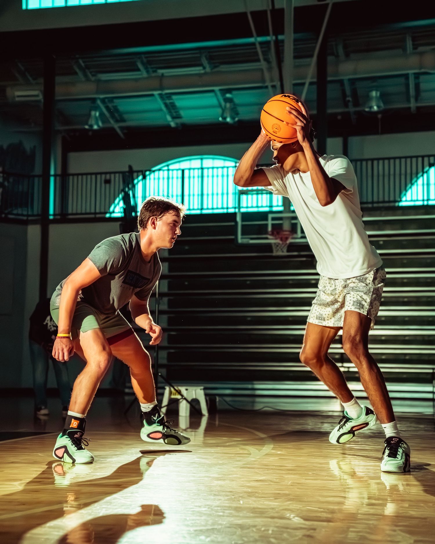 Basketball players practicing dribbling drills in a gymnasium with dramatic lighting.