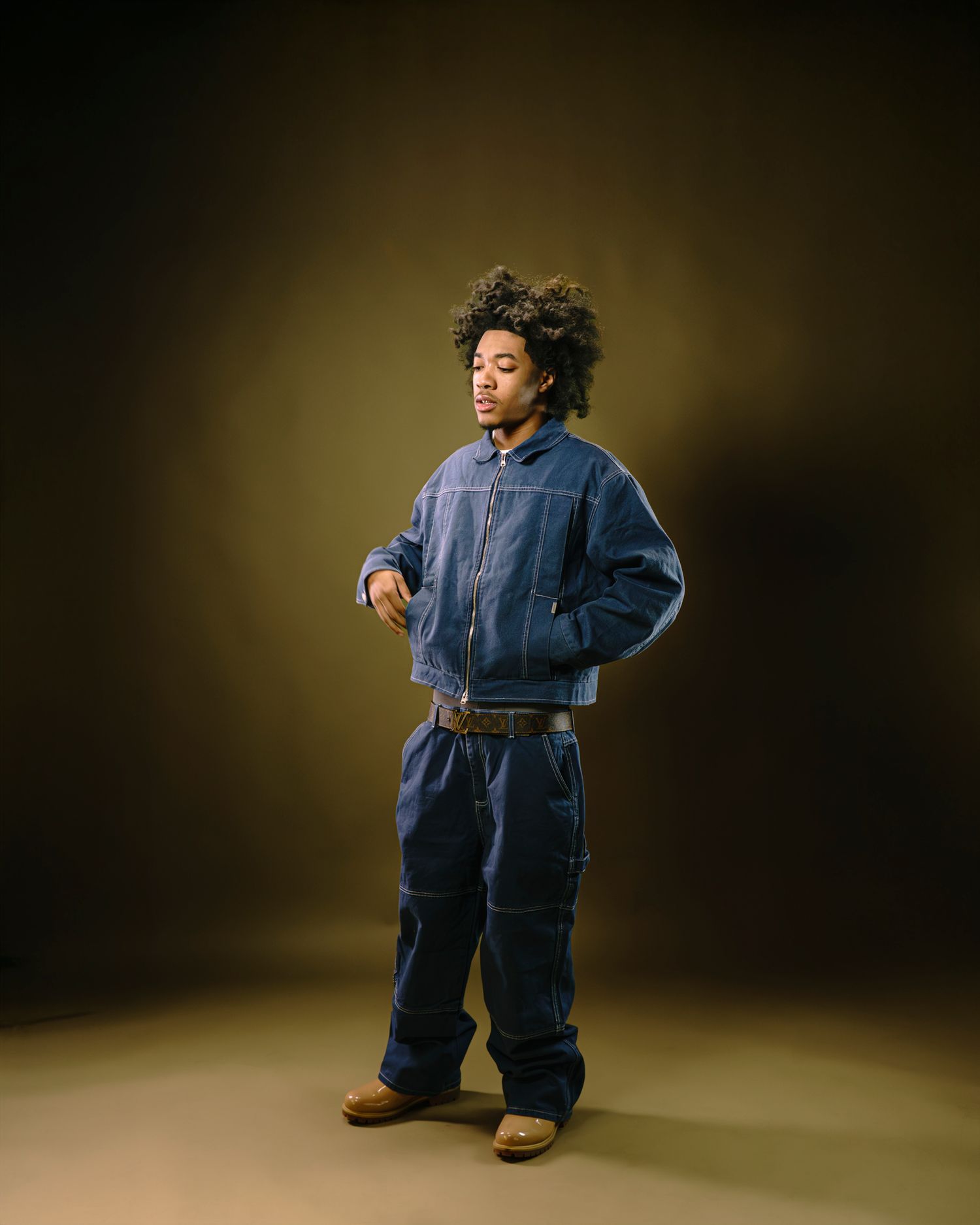 Studio fashion shoot featuring denim jumpsuit outfits against a dark dramatic background.