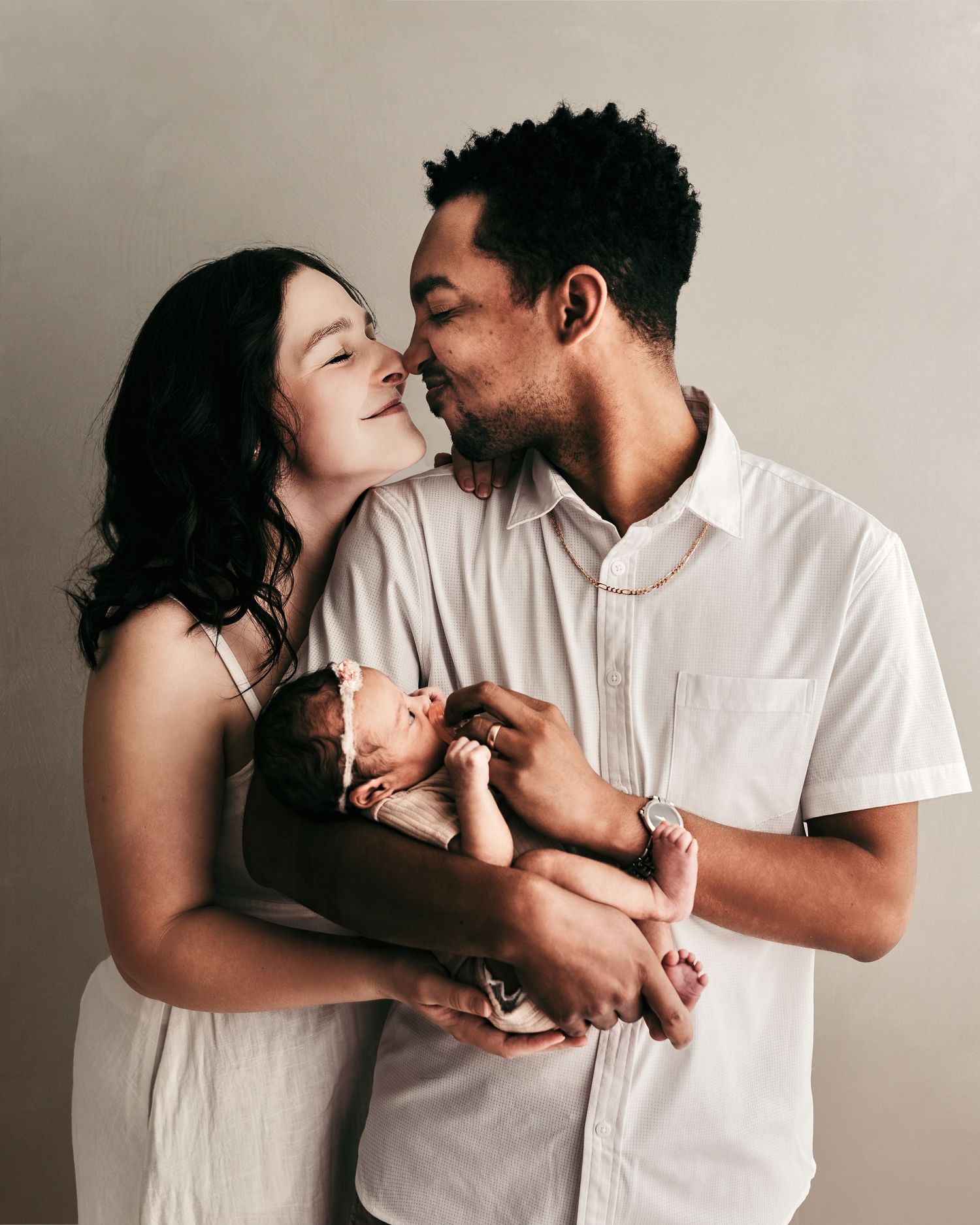 Parents smiling at each other while holding their newborn during a studio newborn photography session.