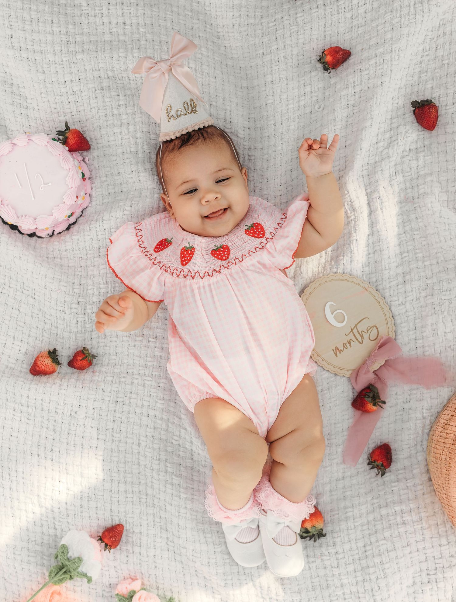 Smiling baby girl surrounded by strawberries during a first birthday milestone photography session near Kansas City.