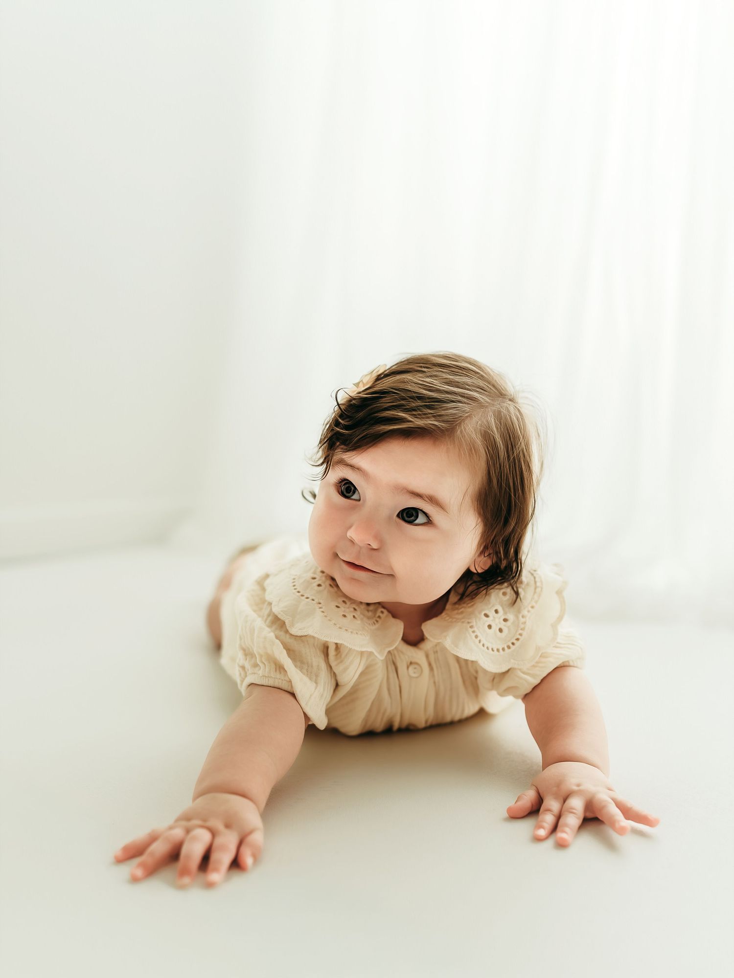 A 6 month old baby girl crawling on a soft white backdrop during a milestone photo session.