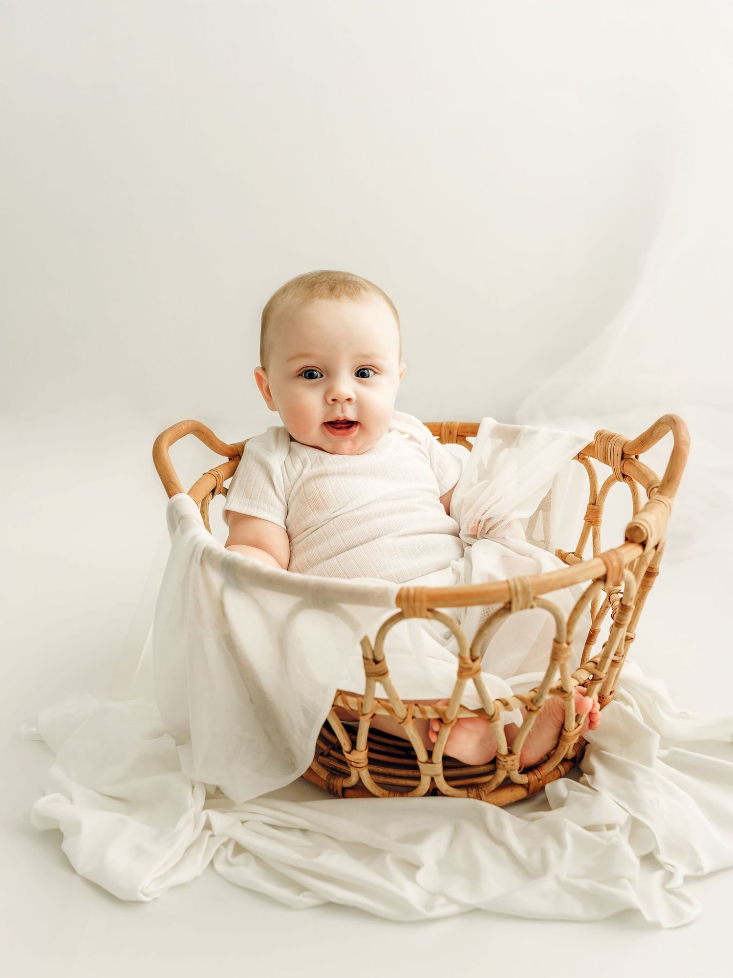 Smiling baby sitting in a wicker basket during a studio milestone photography session.
