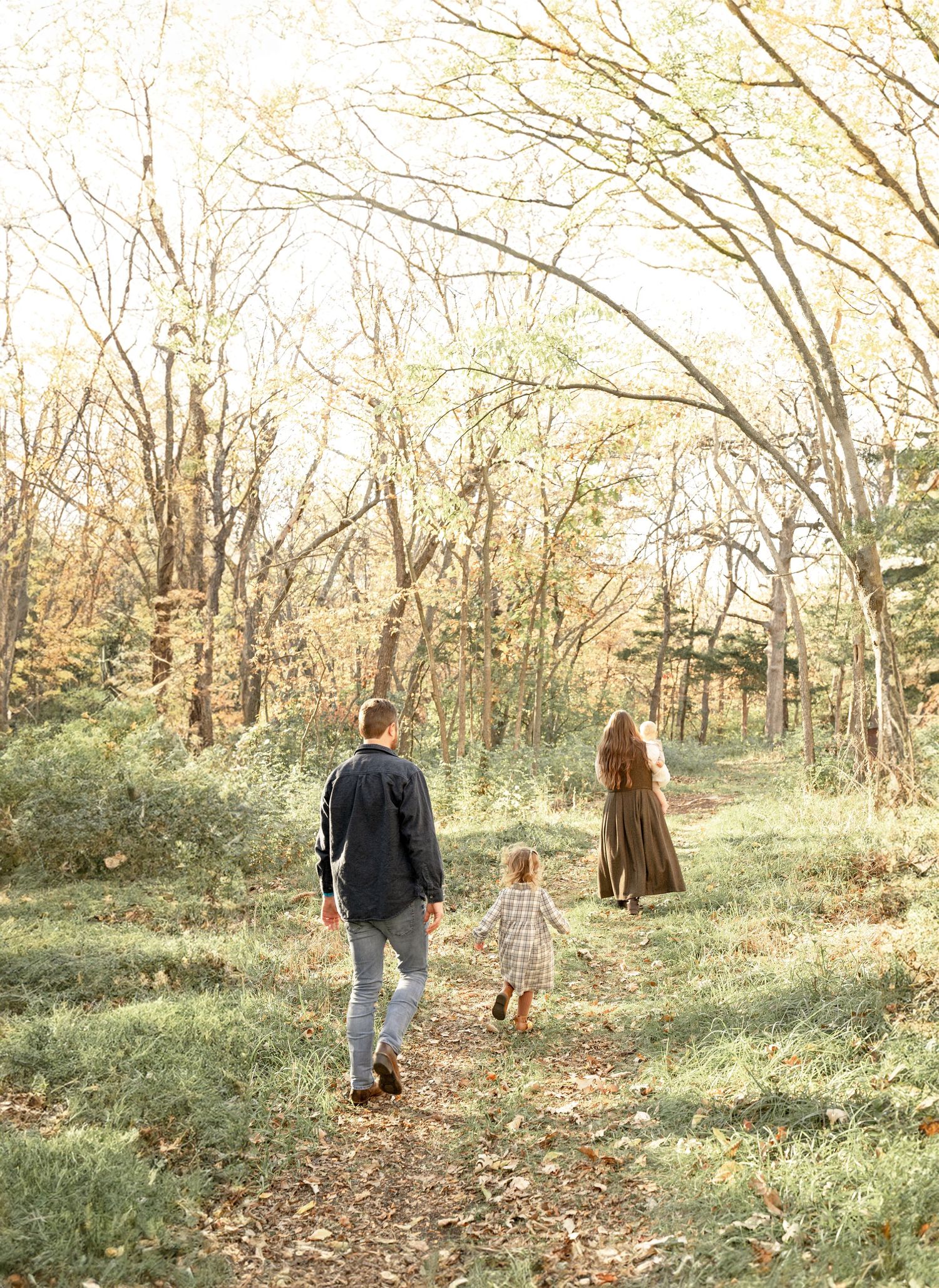 Family walking hand in hand through a sunlit wooded trail during an outdoor family photography session.