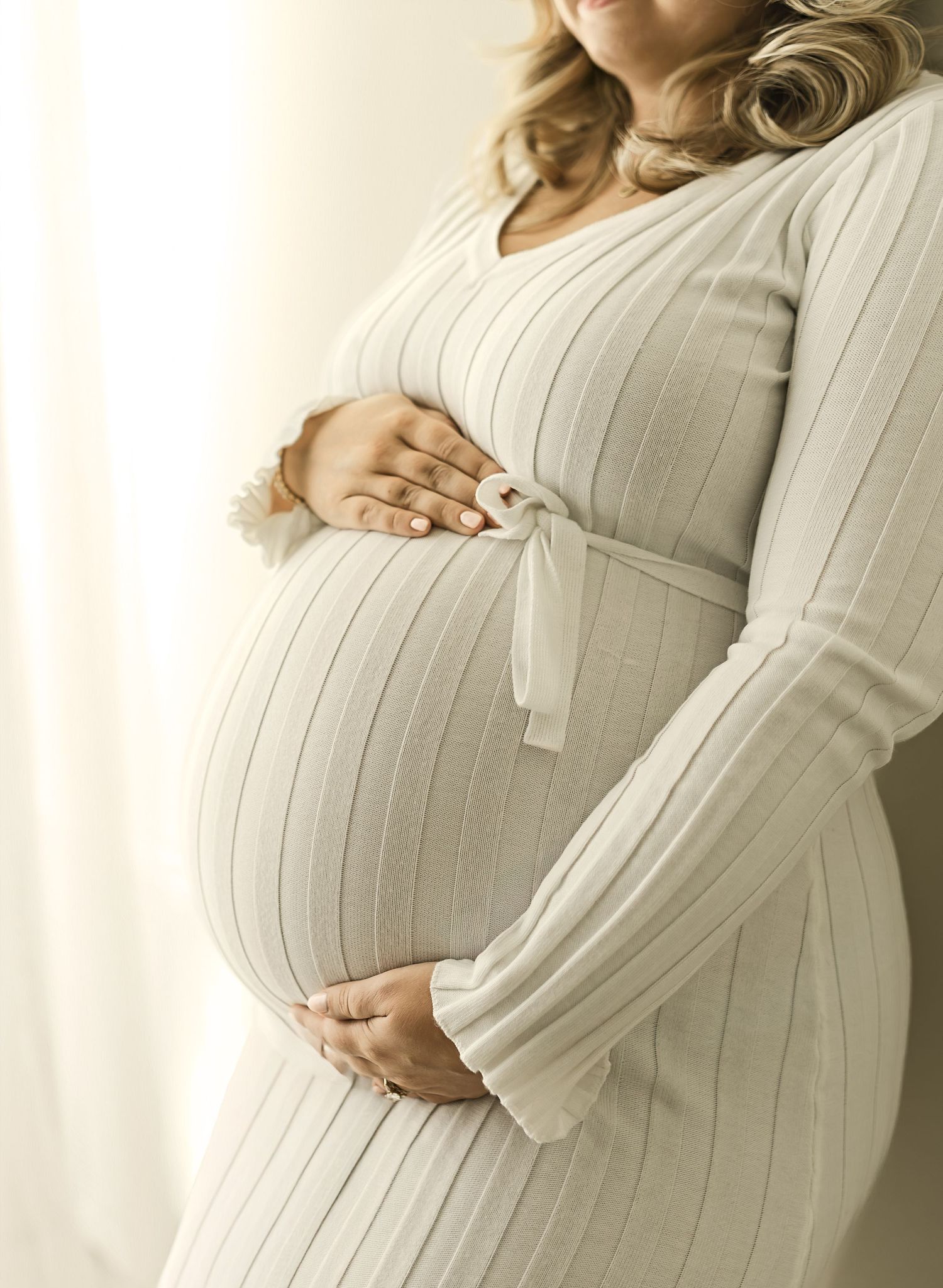Maternity photo series showing a pregnant woman in a white ribbed dress cradling her belly from different angles.