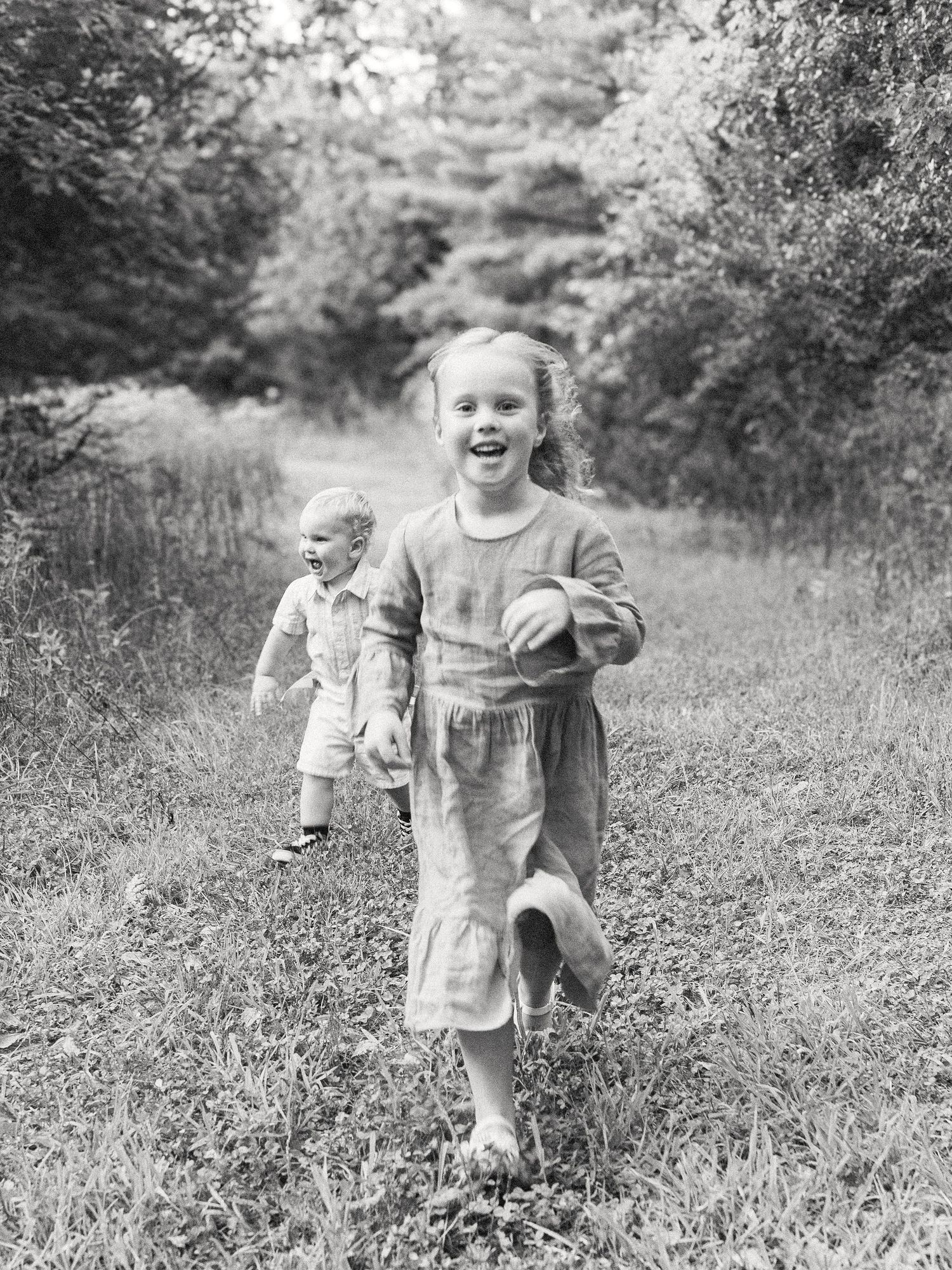 Two children running toward the camera during an outdoor family session, captured in black and white.