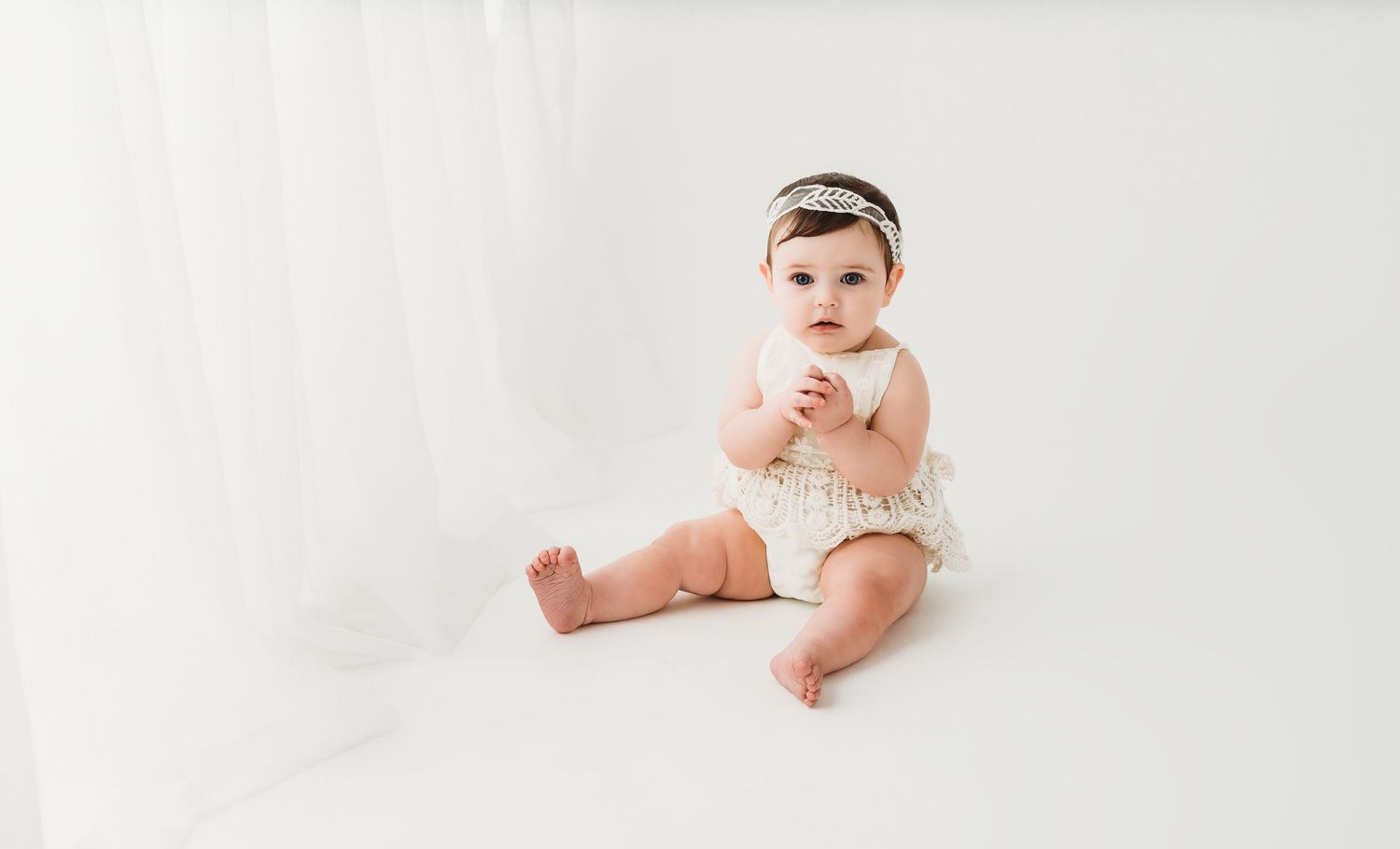 Baby girl milestone portrait sitting on white backdrop with headband in Kansas City photography studio
