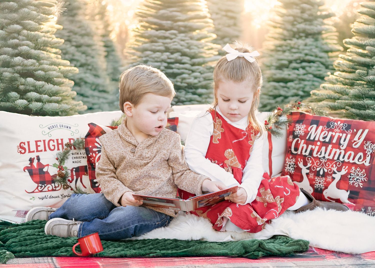 A young boy and girl sit together on a festive blanket, reading a Christmas storybook.