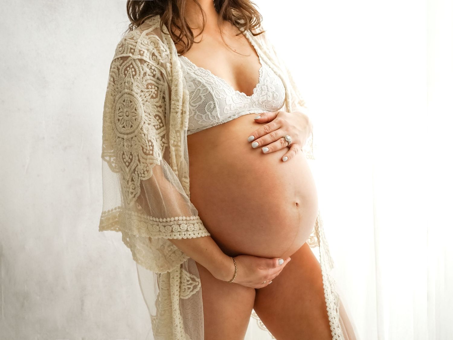 A tender maternity photo showing a pregnant belly in white lingerie with a delicate lace robe.