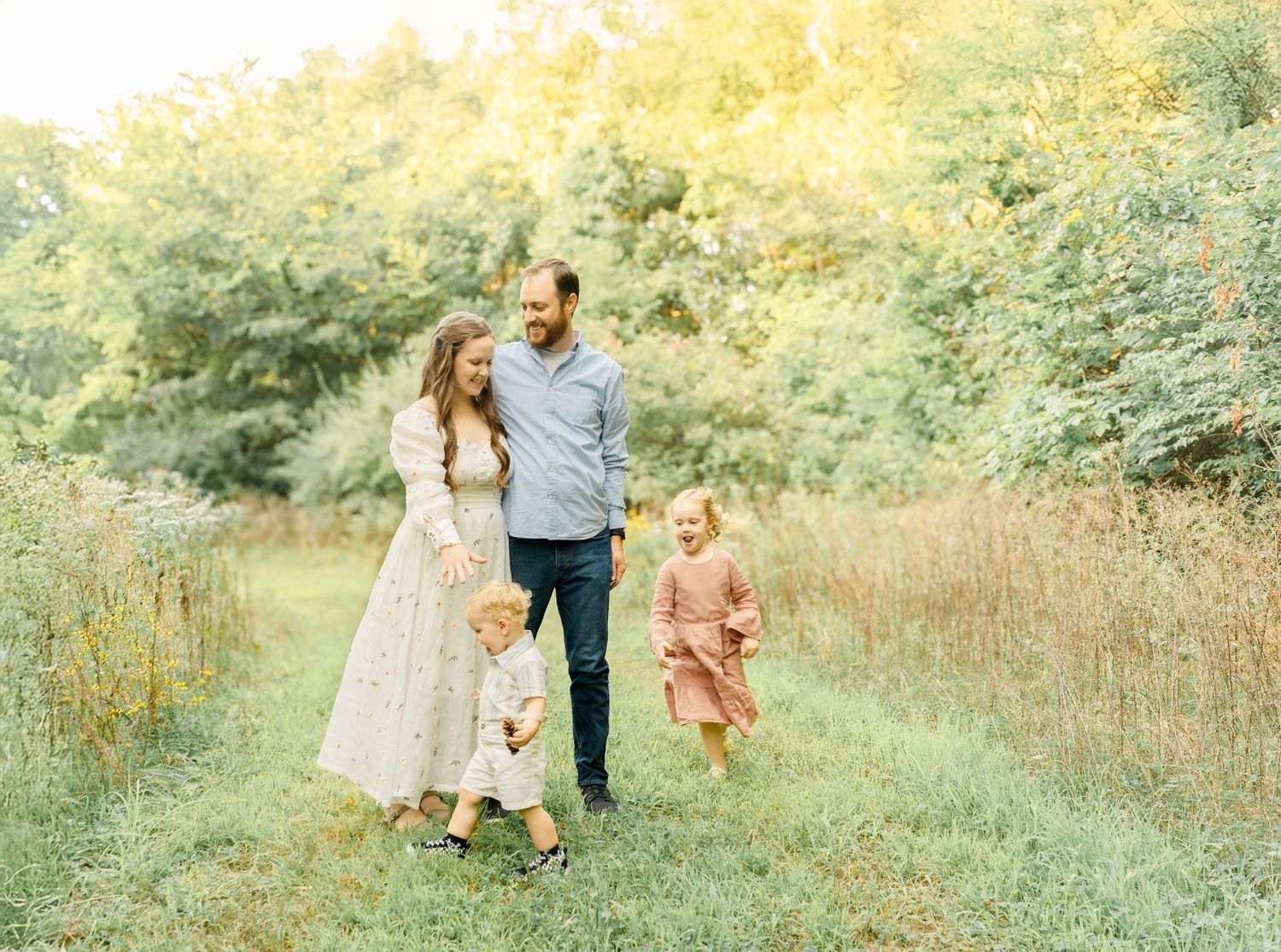 A family of four walking together through a grassy field during an outdoor family photo session in Kansas City.