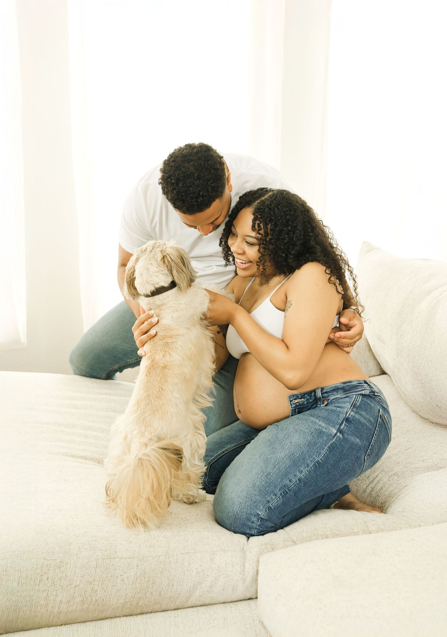 Person sits on white couch cuddling with fluffy golden dog while relaxing in bright sunlit room.