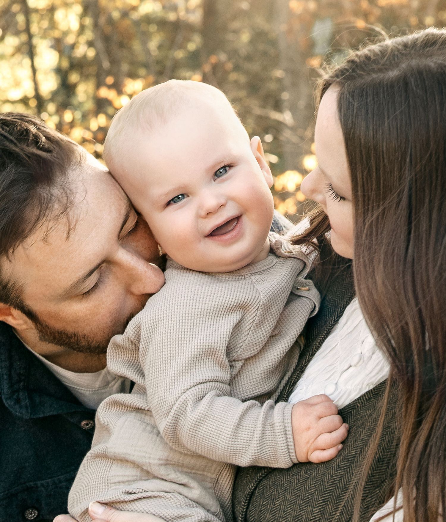 Smiling baby surrounded by loving parents during an outdoor family photography session.