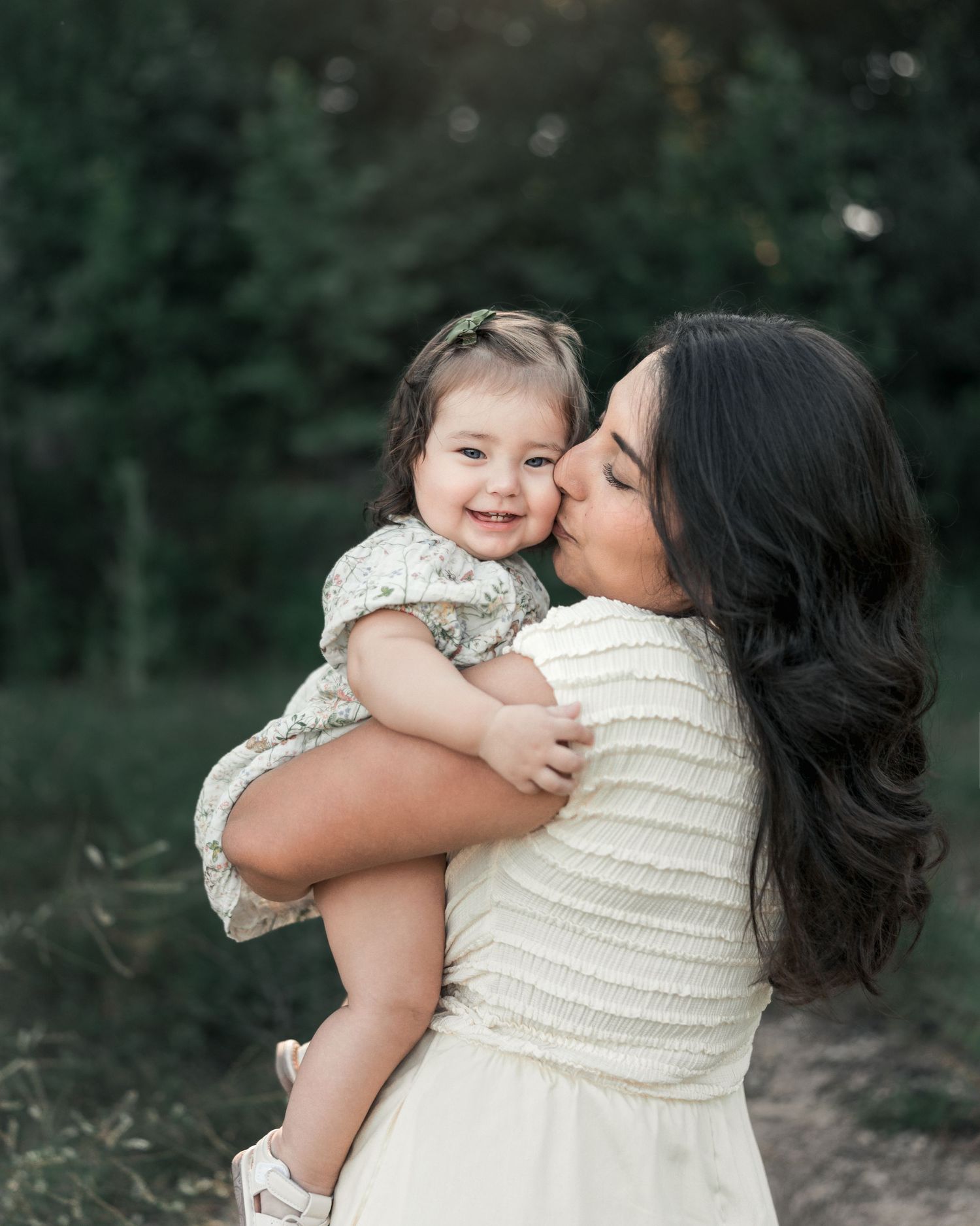 Mother holding her smiling toddler during an outdoor family portrait.