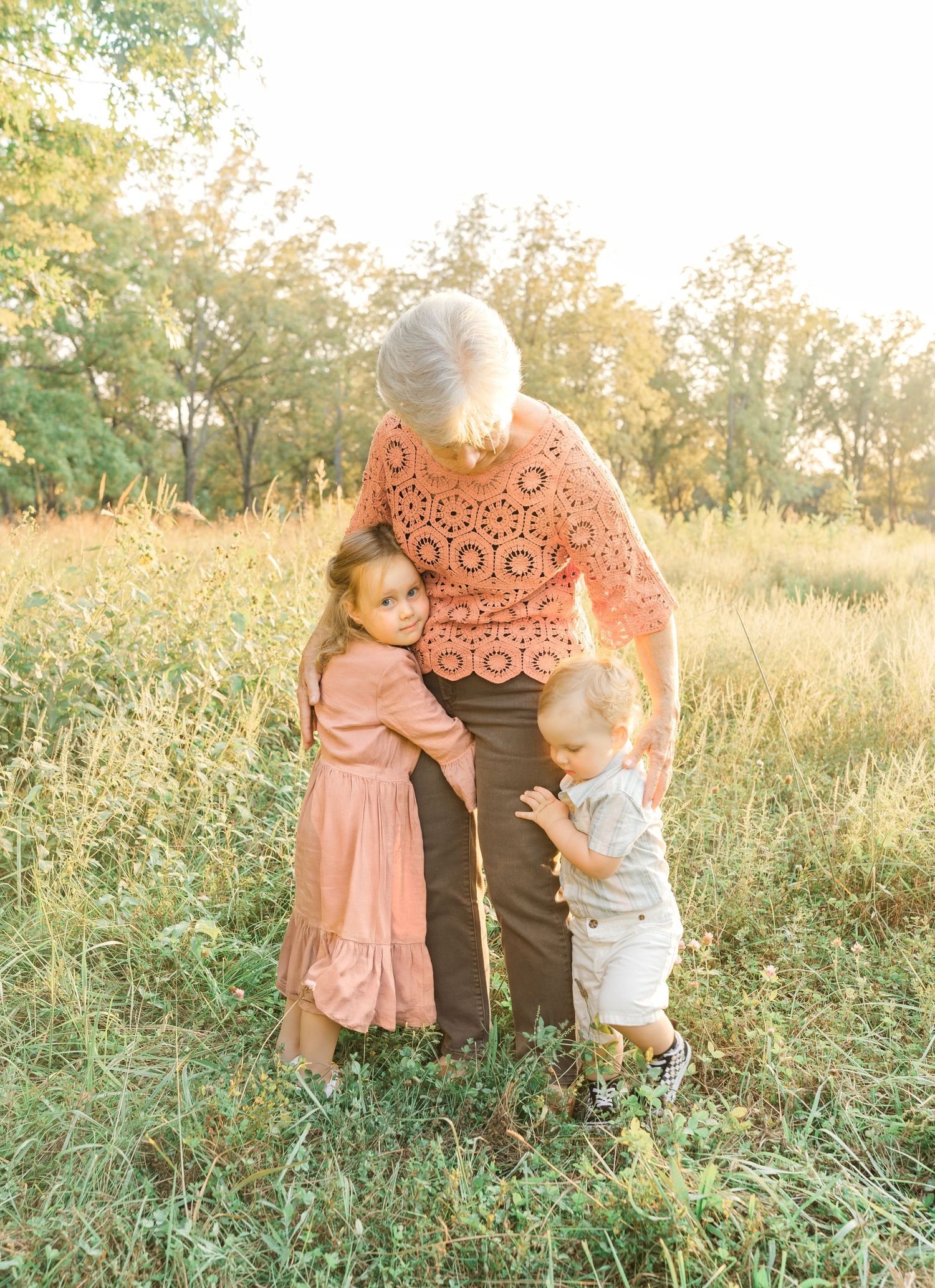 A grandparent standing with two young children in a grassy field during an outdoor family photo session.