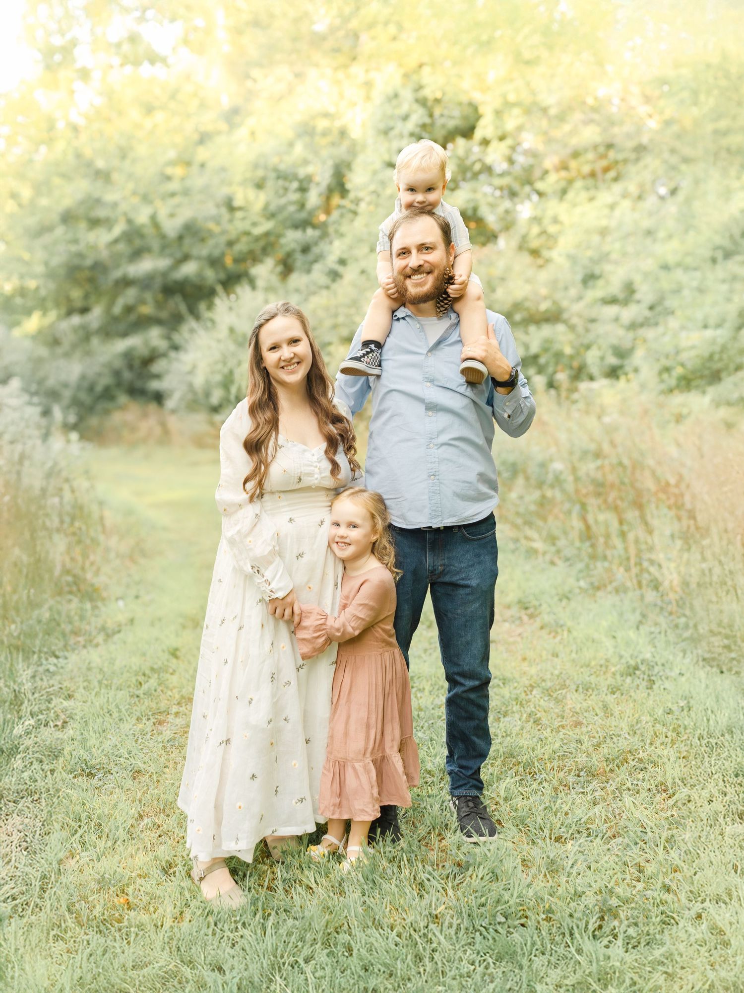 A family of four standing together outdoors with a father holding a child on his shoulders during a Kansas City session.