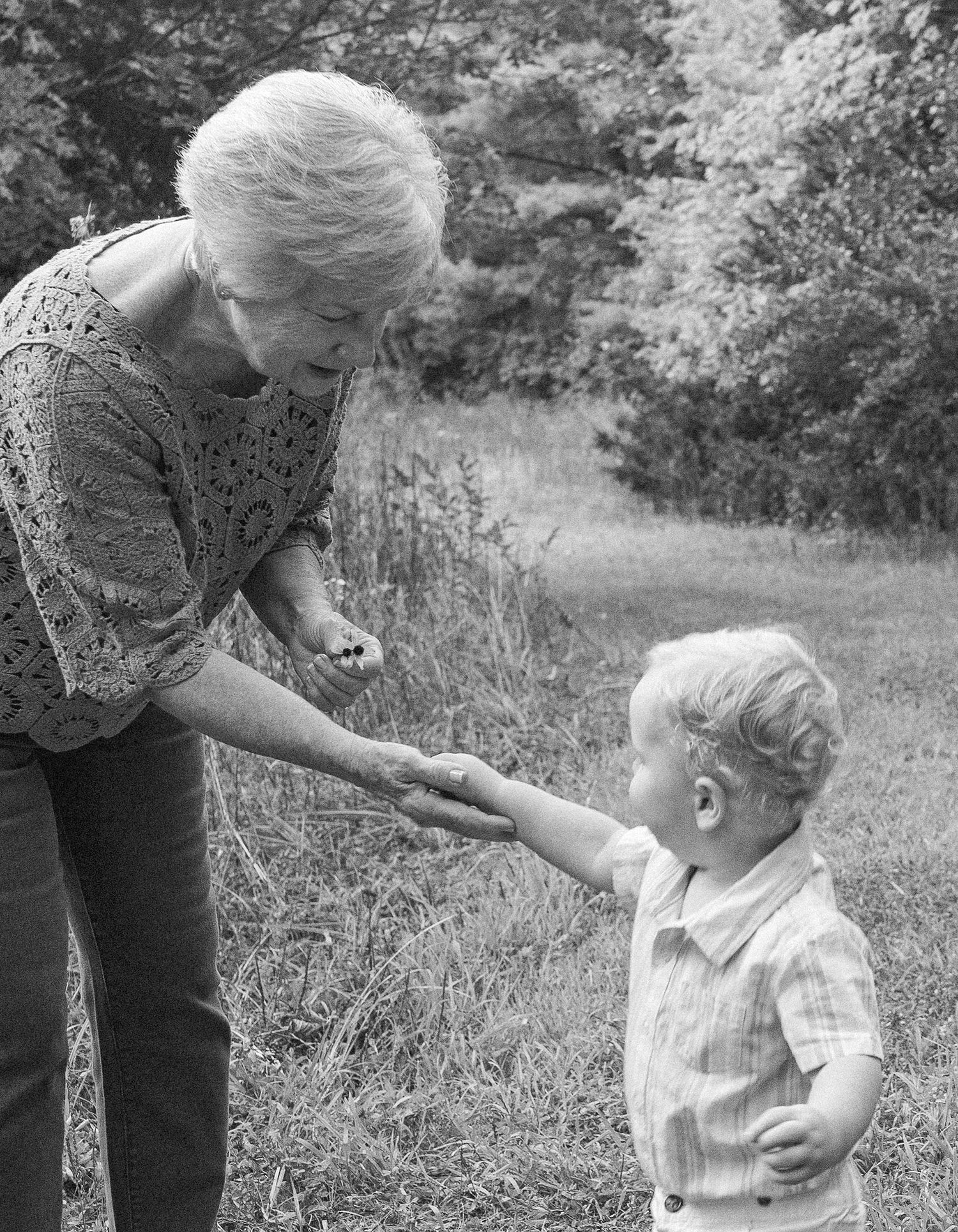 A grandparent holding hands with a young child during an outdoor family session, captured in black and white.