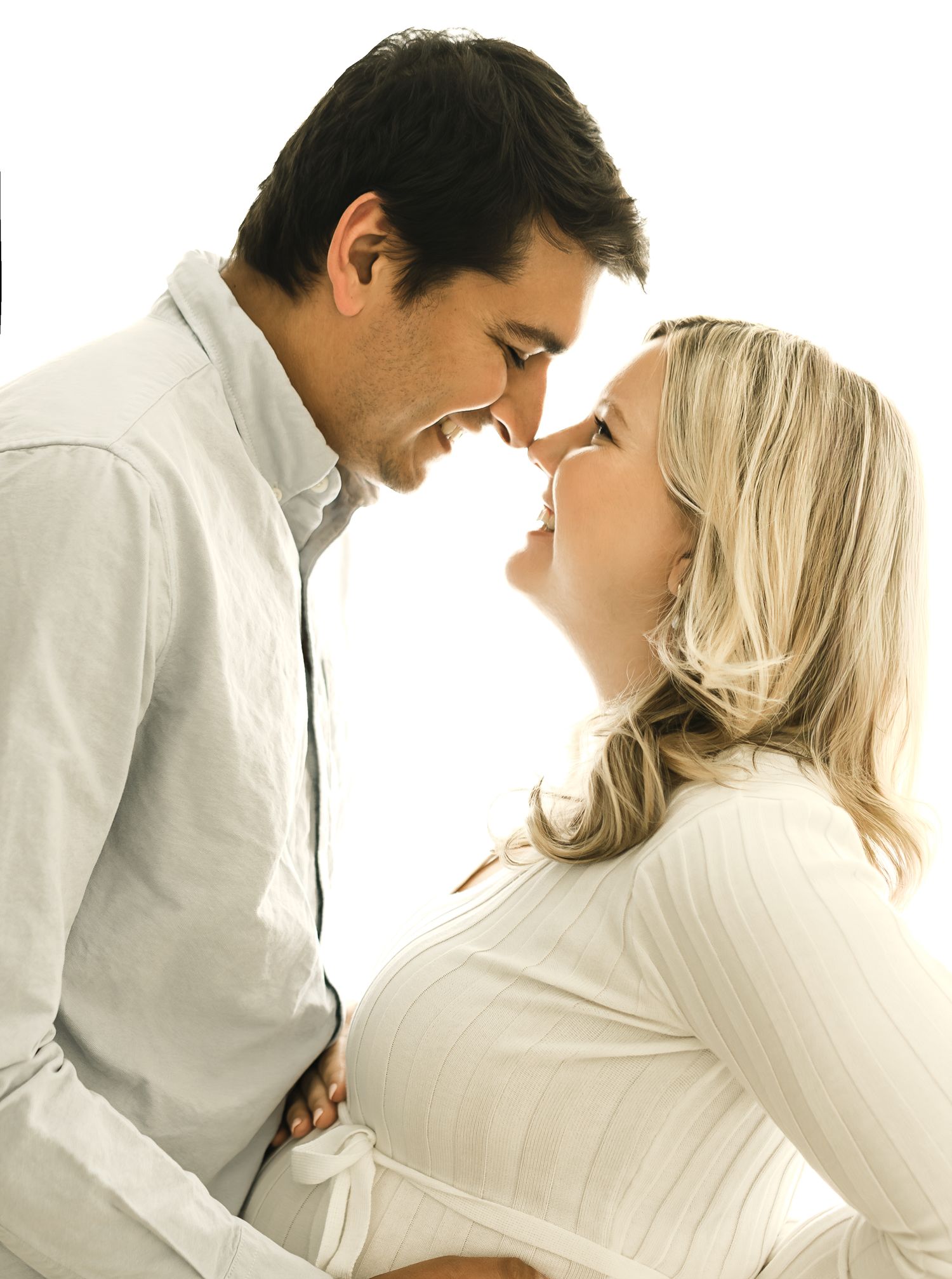 A romantic sequence of a couple in white clothing embracing and kissing against a bright background.