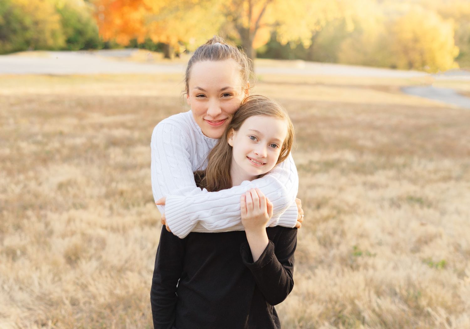 Two people embracing and smiling in a field during golden hour with autumn colors in the background.
