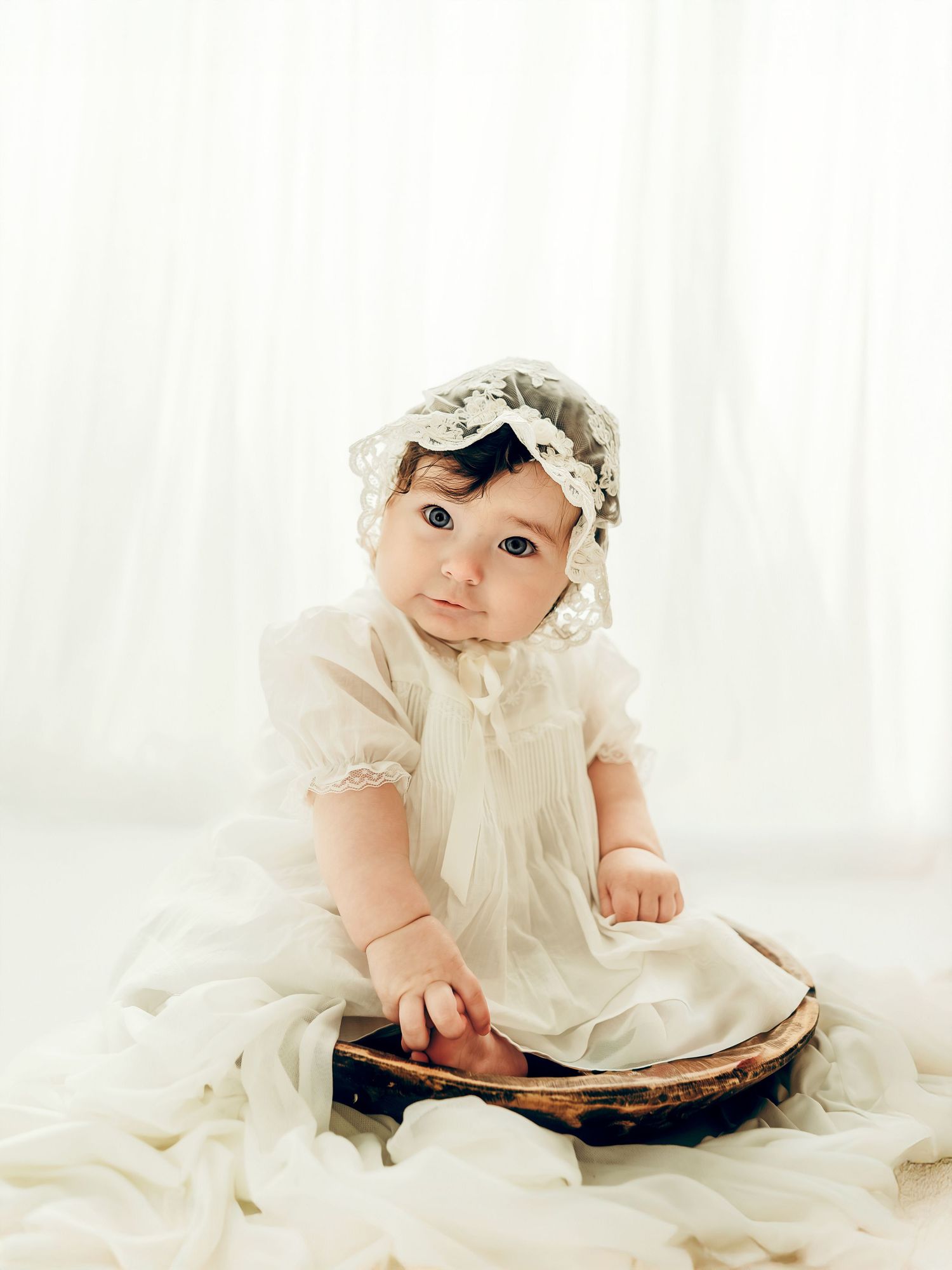 A 6 month old baby girl sitting on a soft blanket in a bowl during a neutral milestone photo session.
