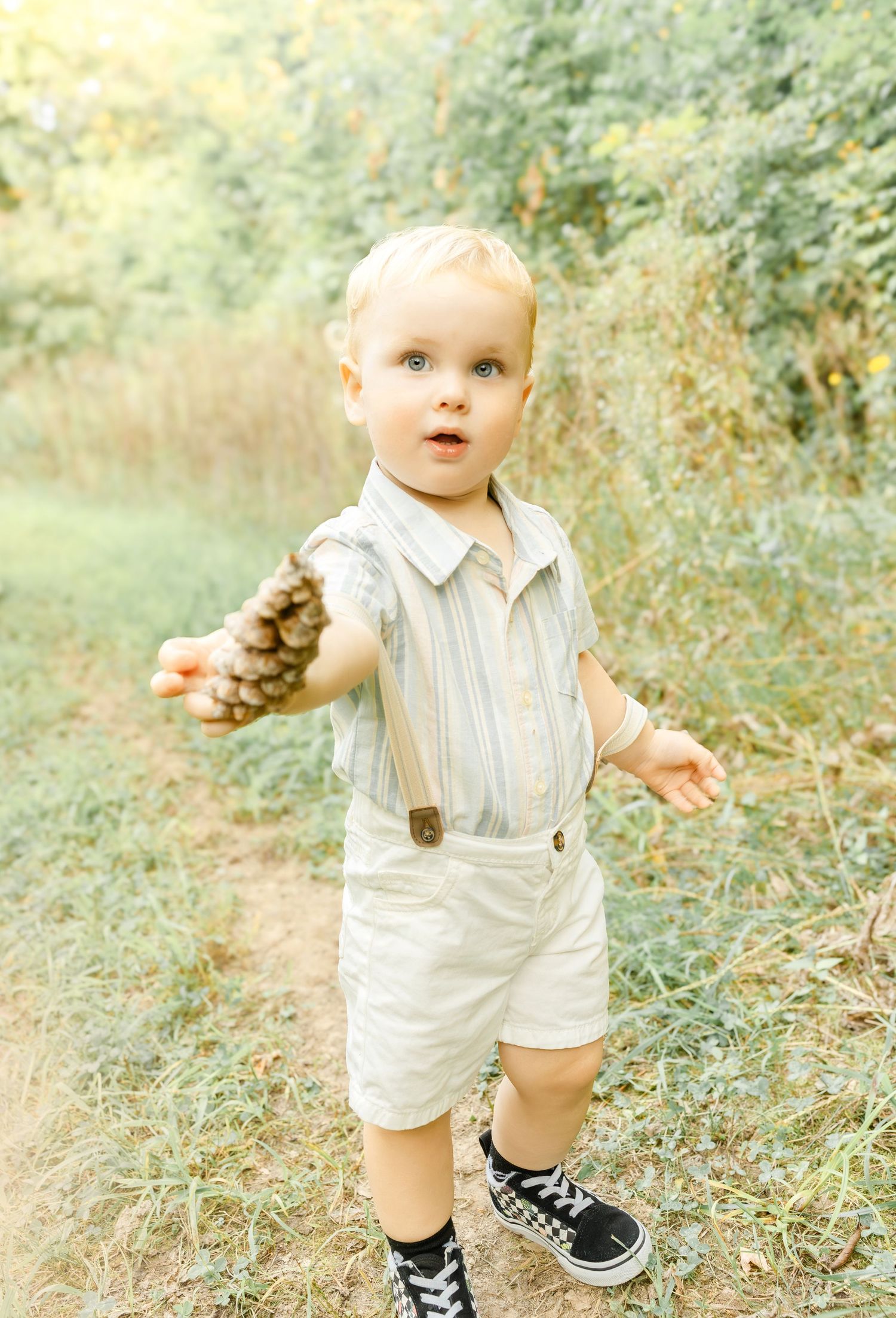A young boy walking through a grassy field holding flowers during an outdoor family photo session.