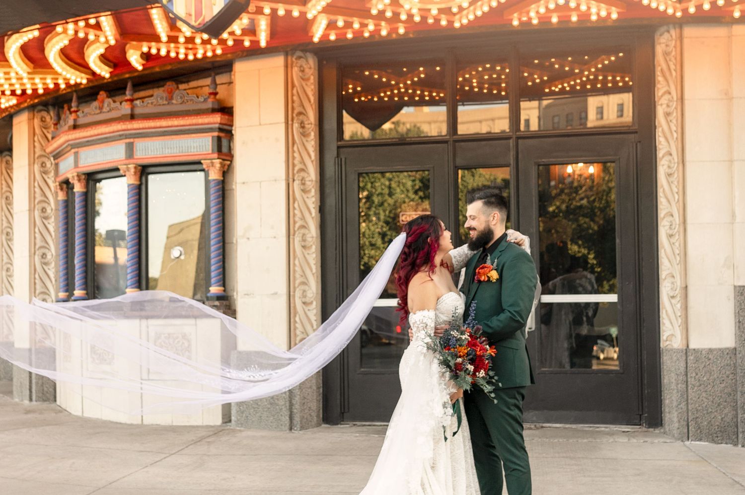 A couple shares a romantic moment outside a historic storefront decorated with string lights as a flowing veil catches the breeze.