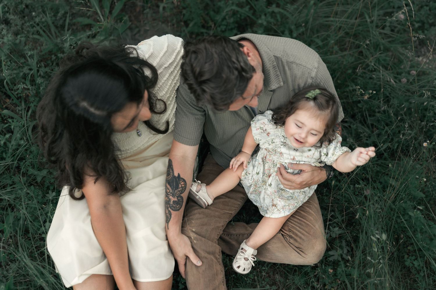 Overhead portrait of a family laughing together in tall grass during an outdoor session.