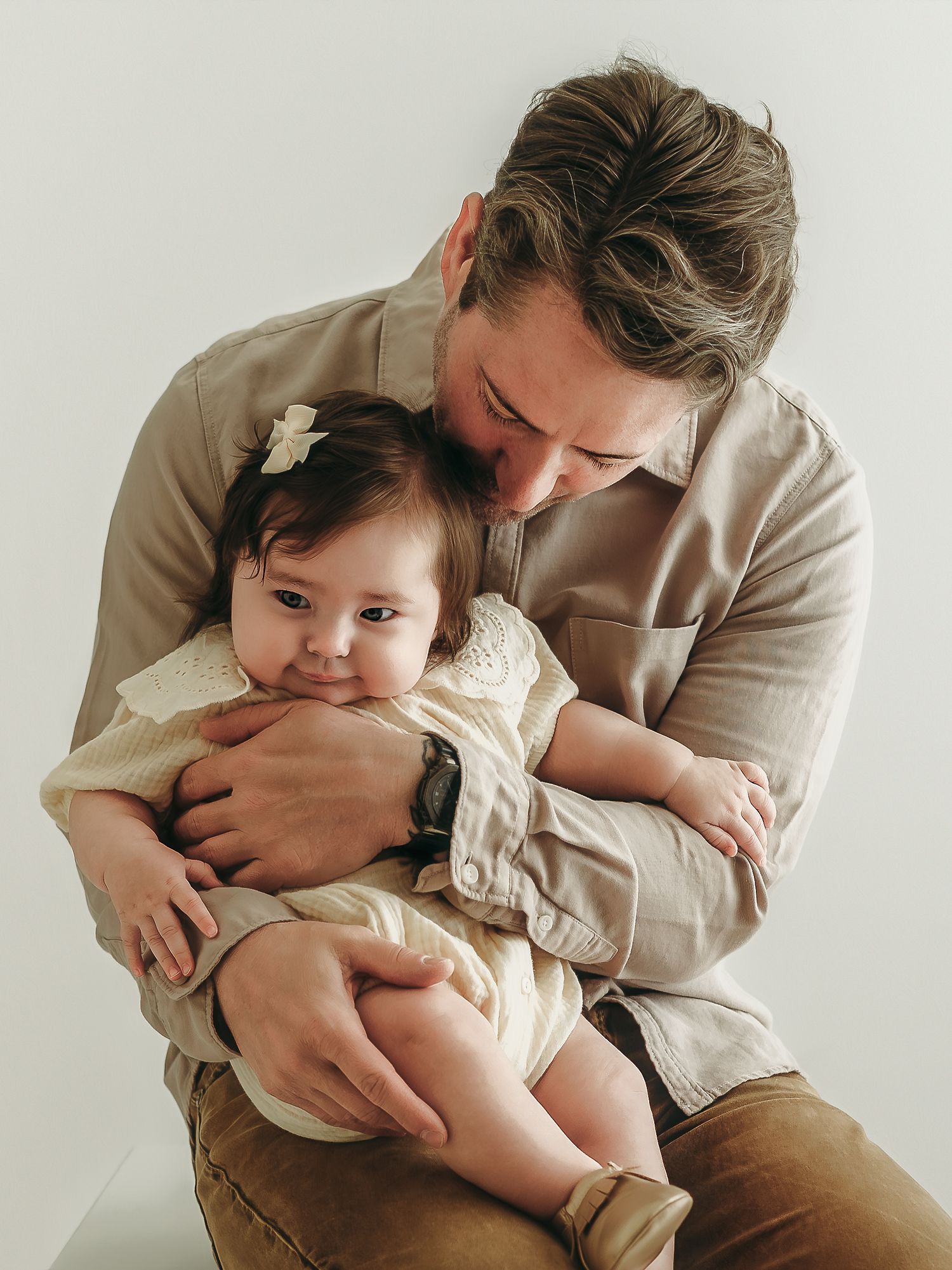 A father holding his baby girl close during a calm, intimate moment in a studio photo session.