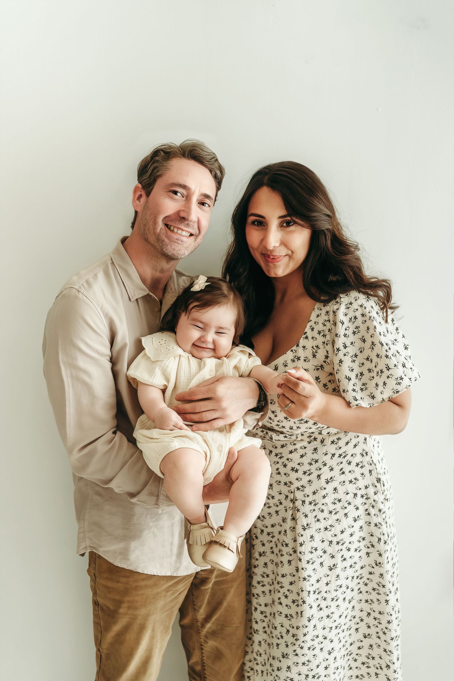 A smiling family of three holding their baby girl during a studio milestone session.