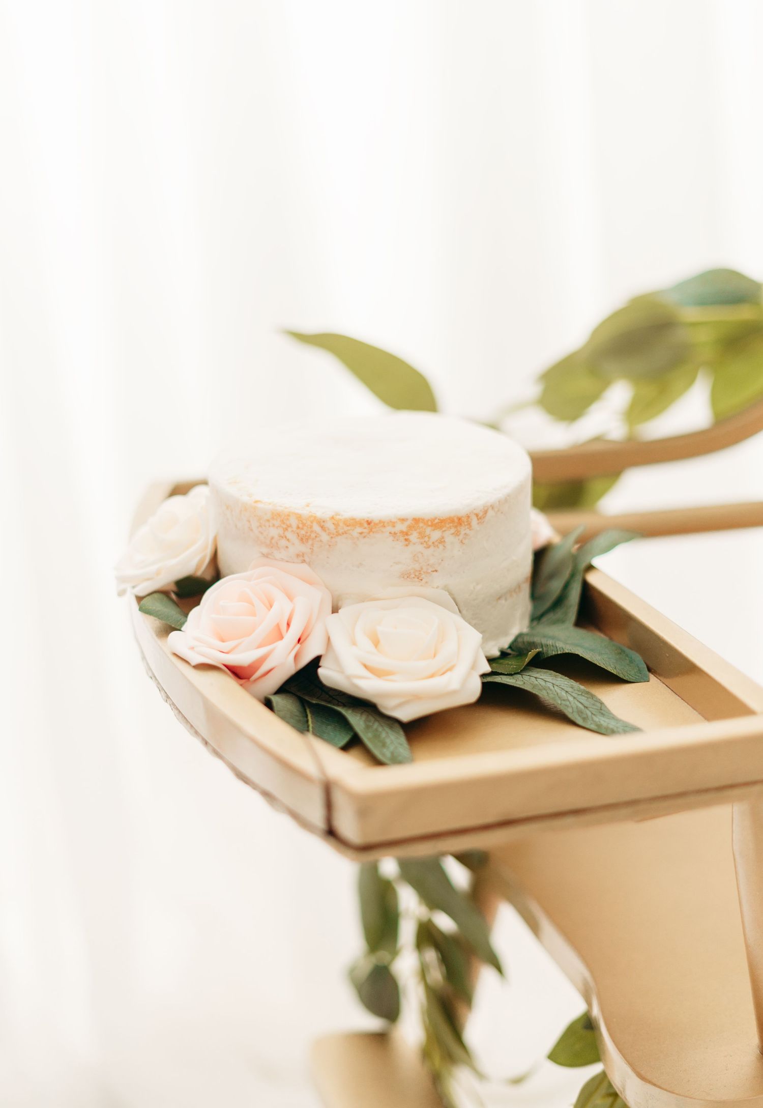Simple white cake with delicate peach and cream roses on wooden serving tray against light background.