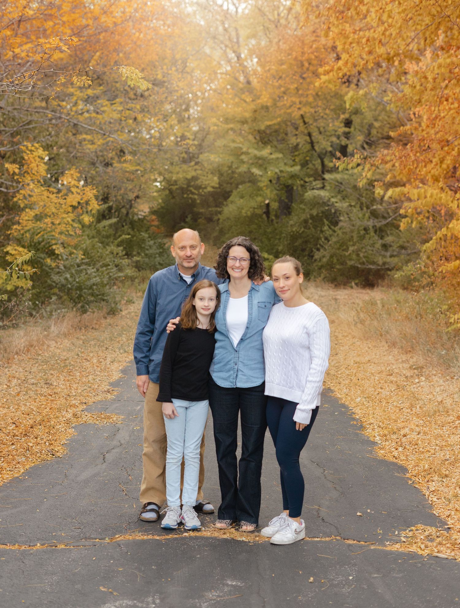 A family poses together on a path surrounded by vibrant fall foliage and golden autumn leaves in Kansas City