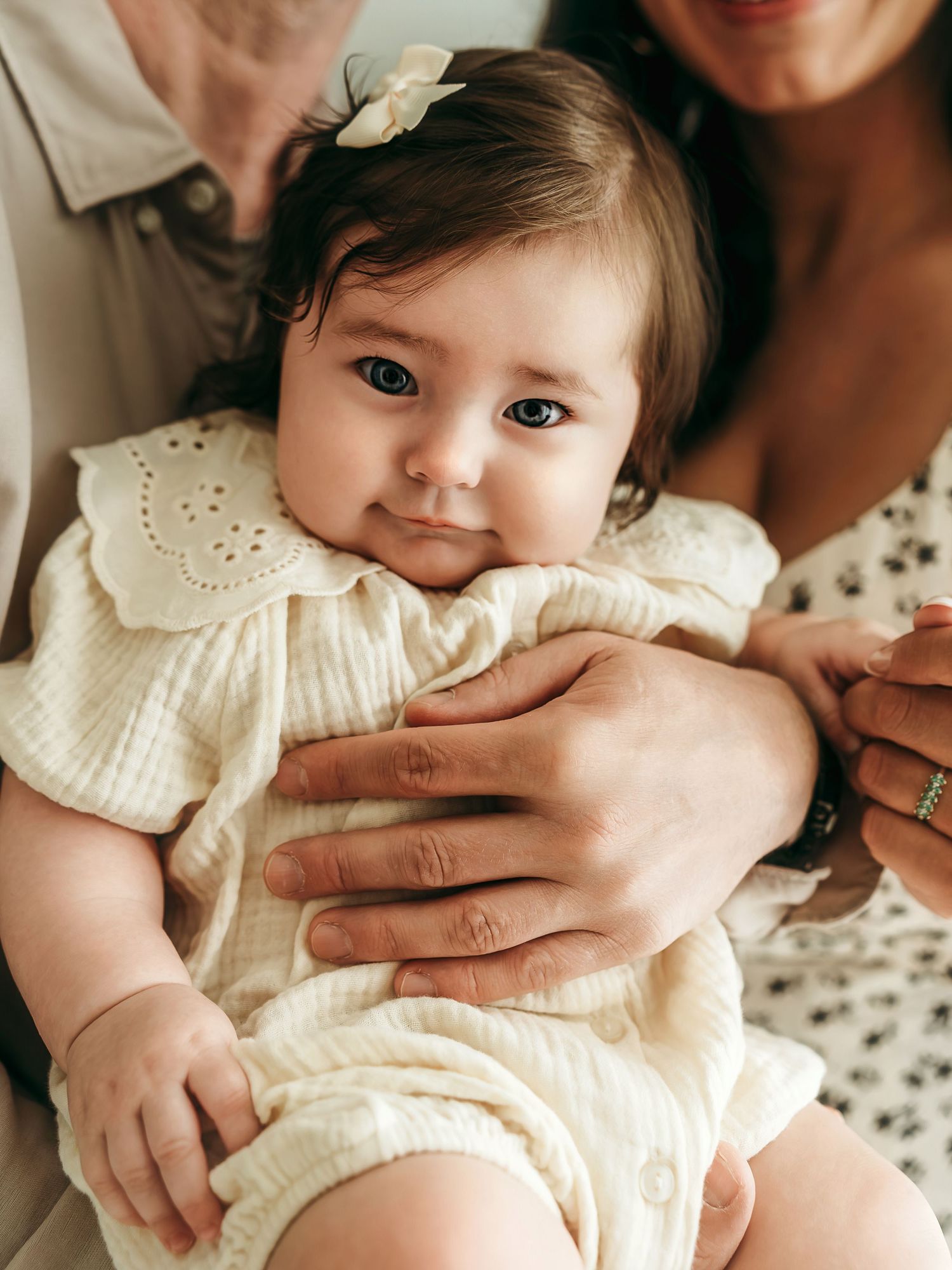 A baby girl sitting in her parents’ arms during a warm, natural milestone photo session.