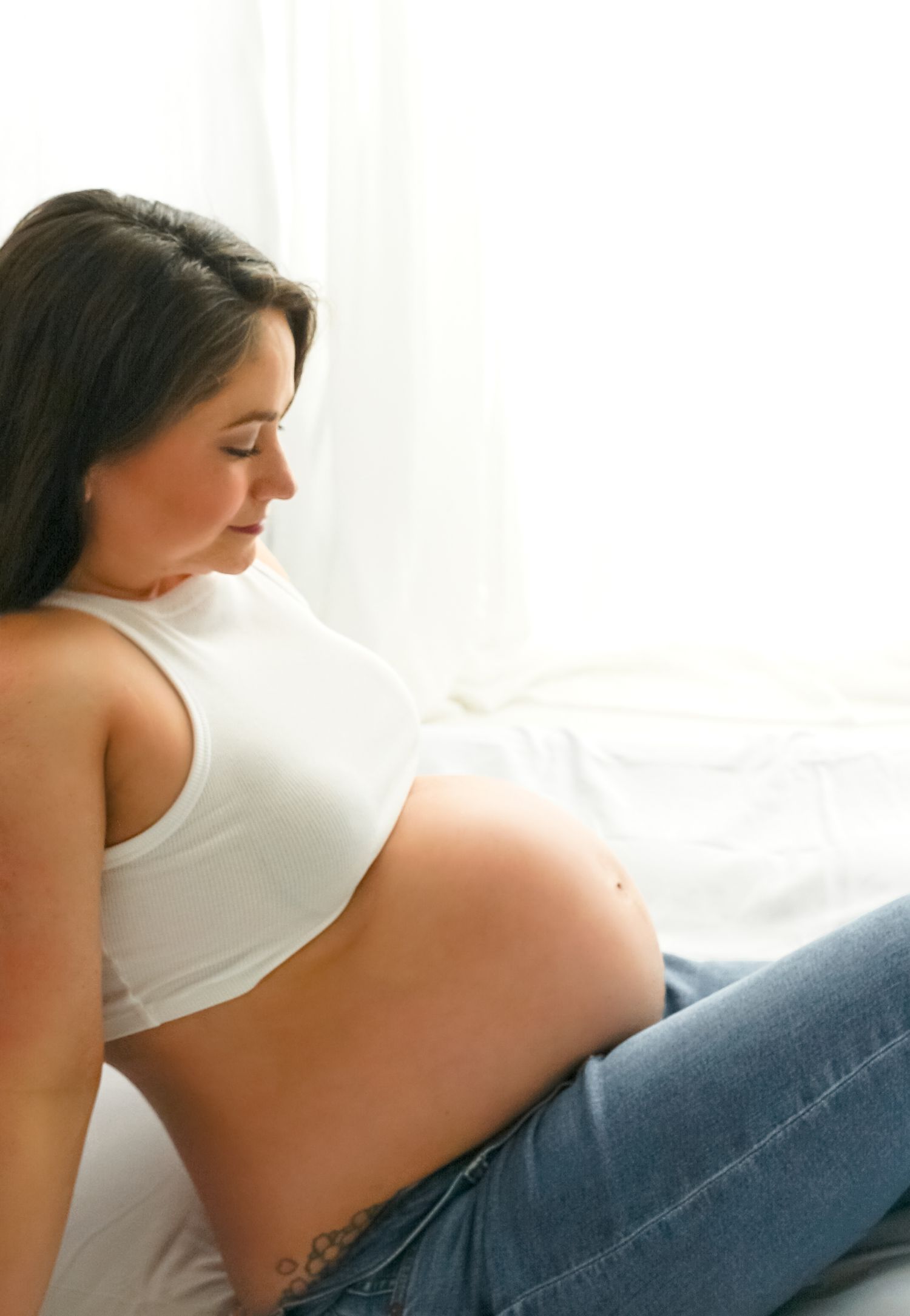 A pregnant woman in a white top rests peacefully on a blue couch in a brightly lit room.