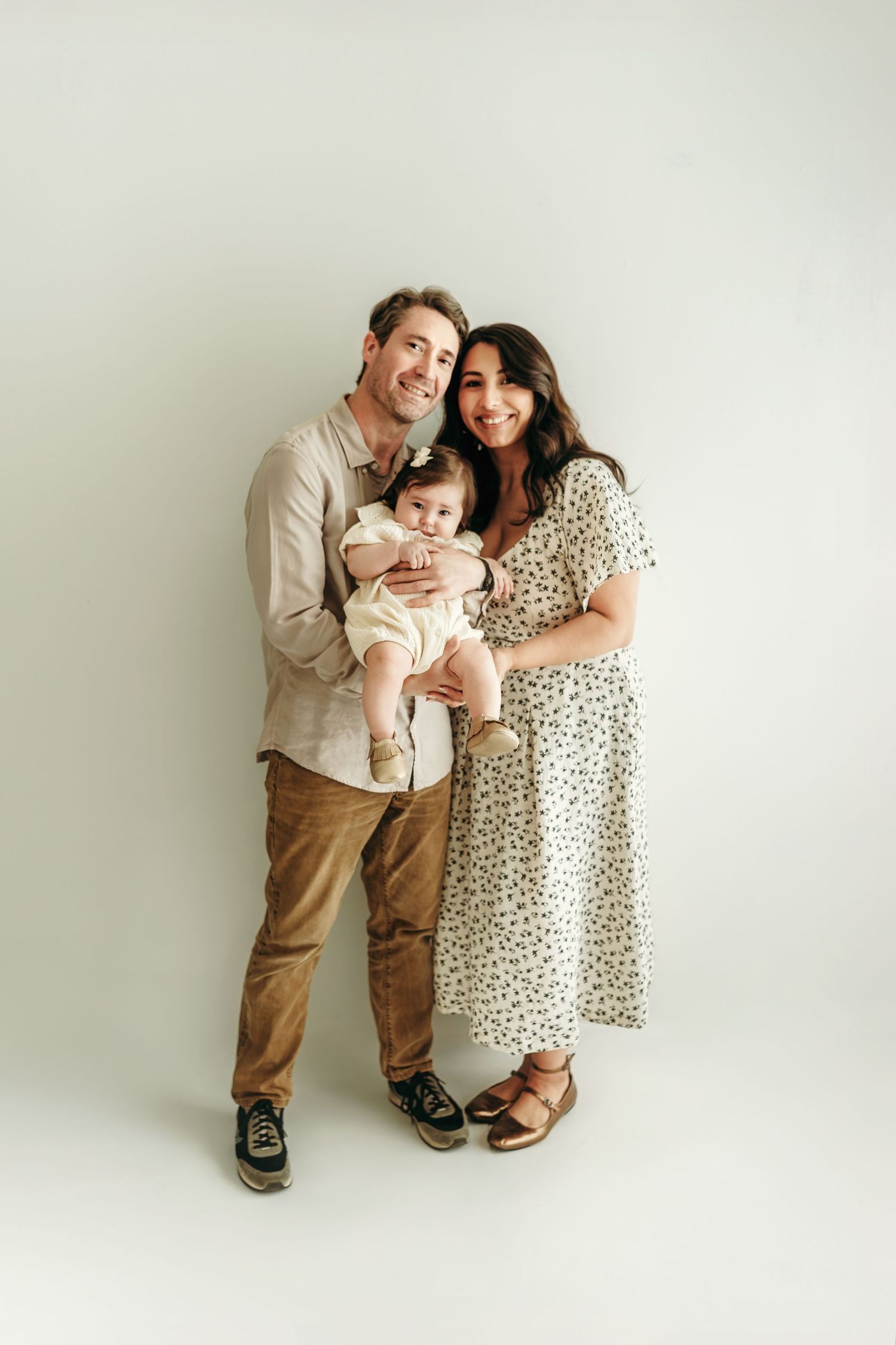 A family of three standing together with their baby during a neutral Kansas City studio photo session.