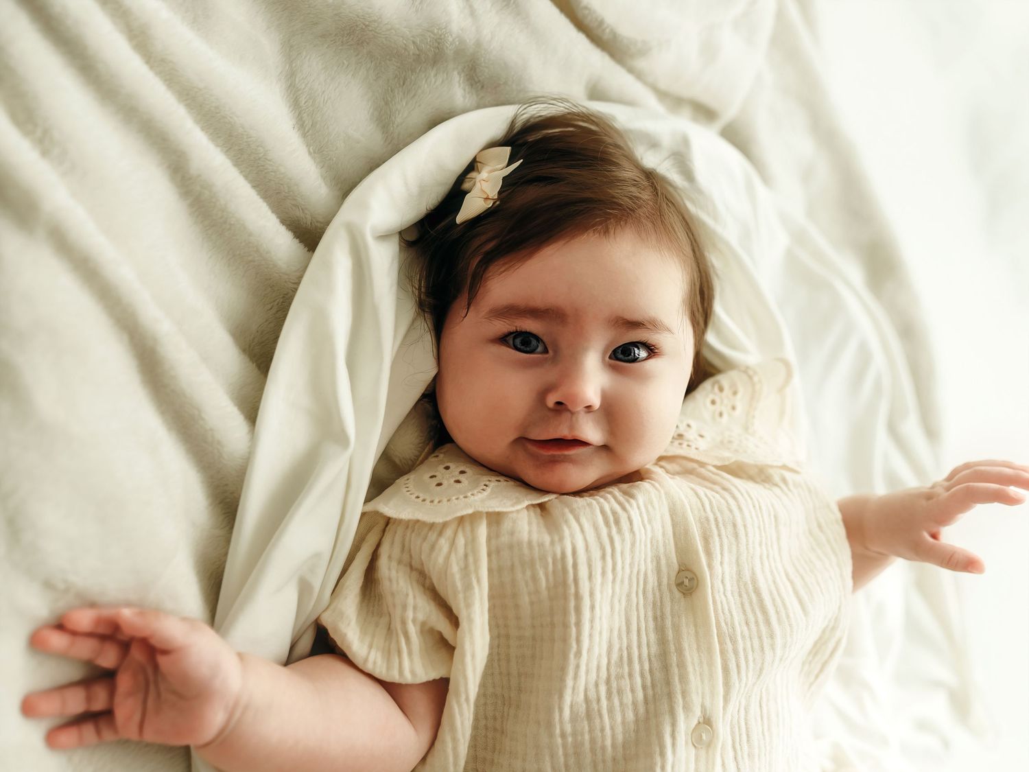 A 6 month old baby girl lying on a soft neutral blanket, smiling during a milestone photo session.