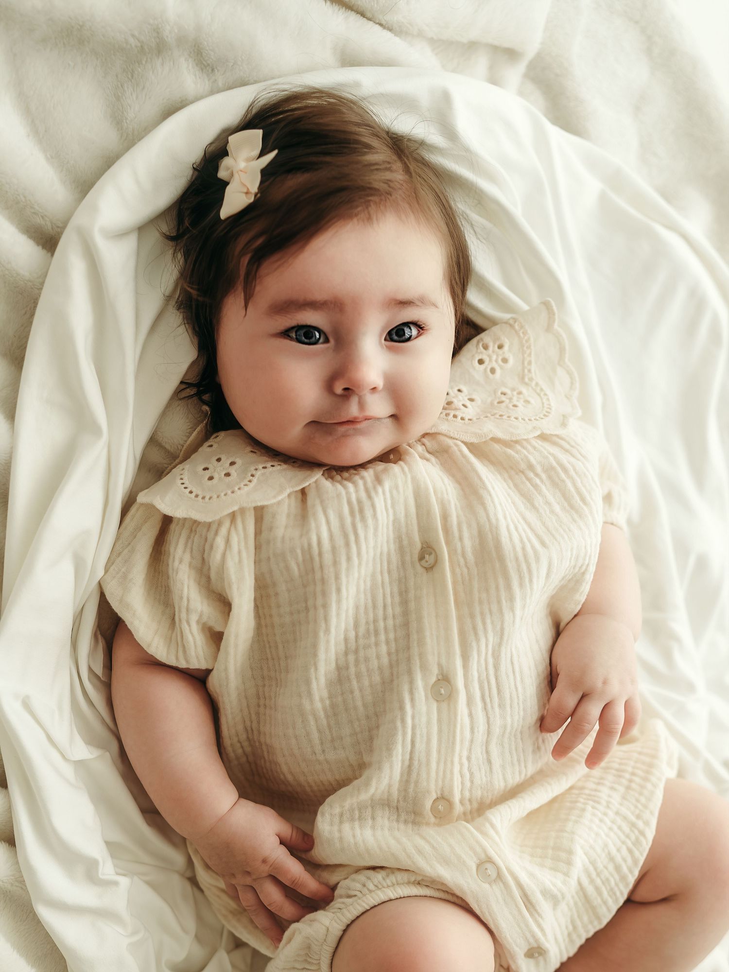 A 6 month old baby girl lying on a soft blanket, smiling during a milestone photo session.