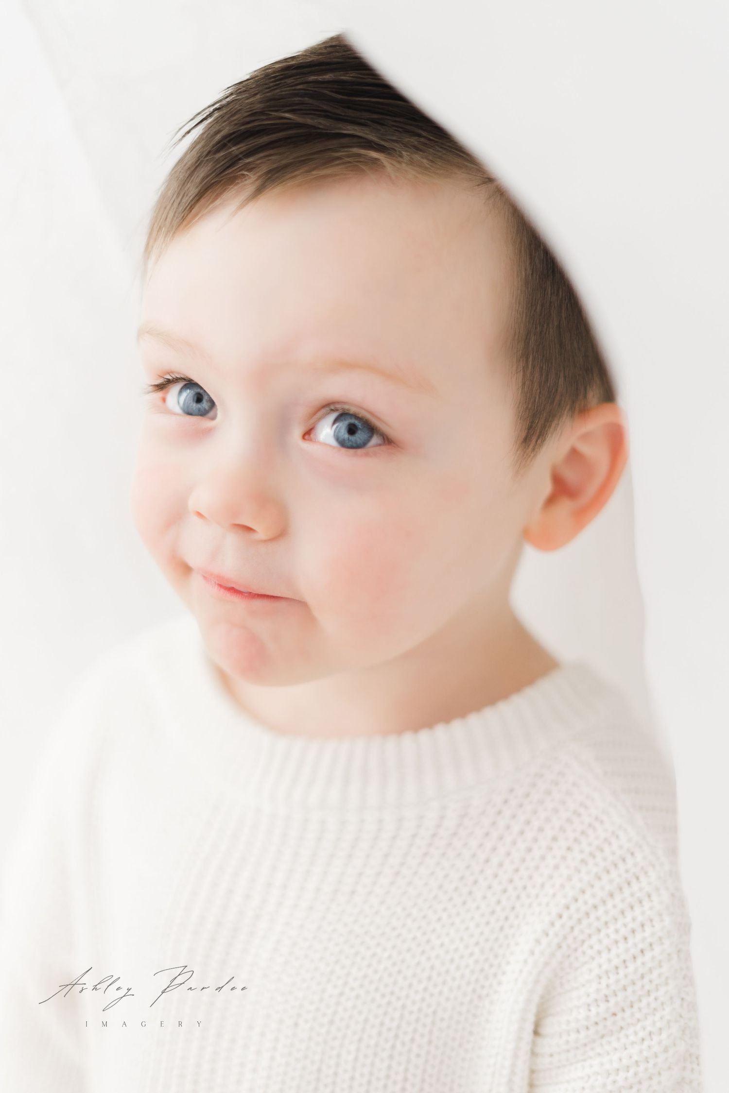 A young child wearing a white knit sweater poses for a soft, ethereal portrait against a light background.
