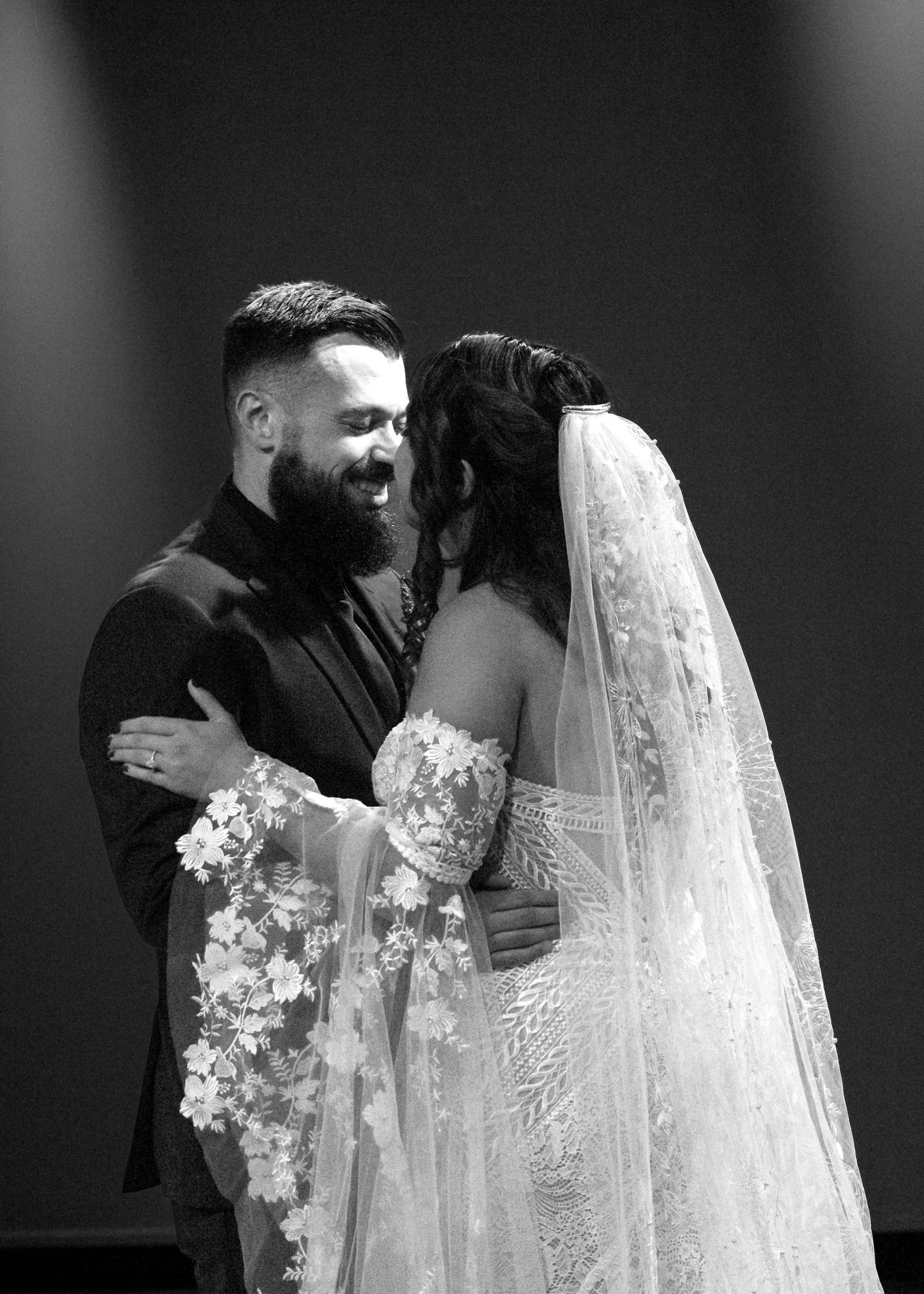 A black and white wedding photograph captures an intimate moment as a couple shares a joyful laugh during their ceremony.