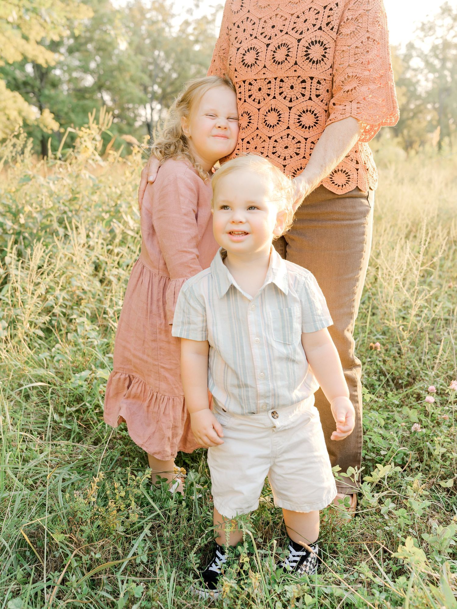 Two young children standing together during a golden hour outdoor family session in a grassy field.