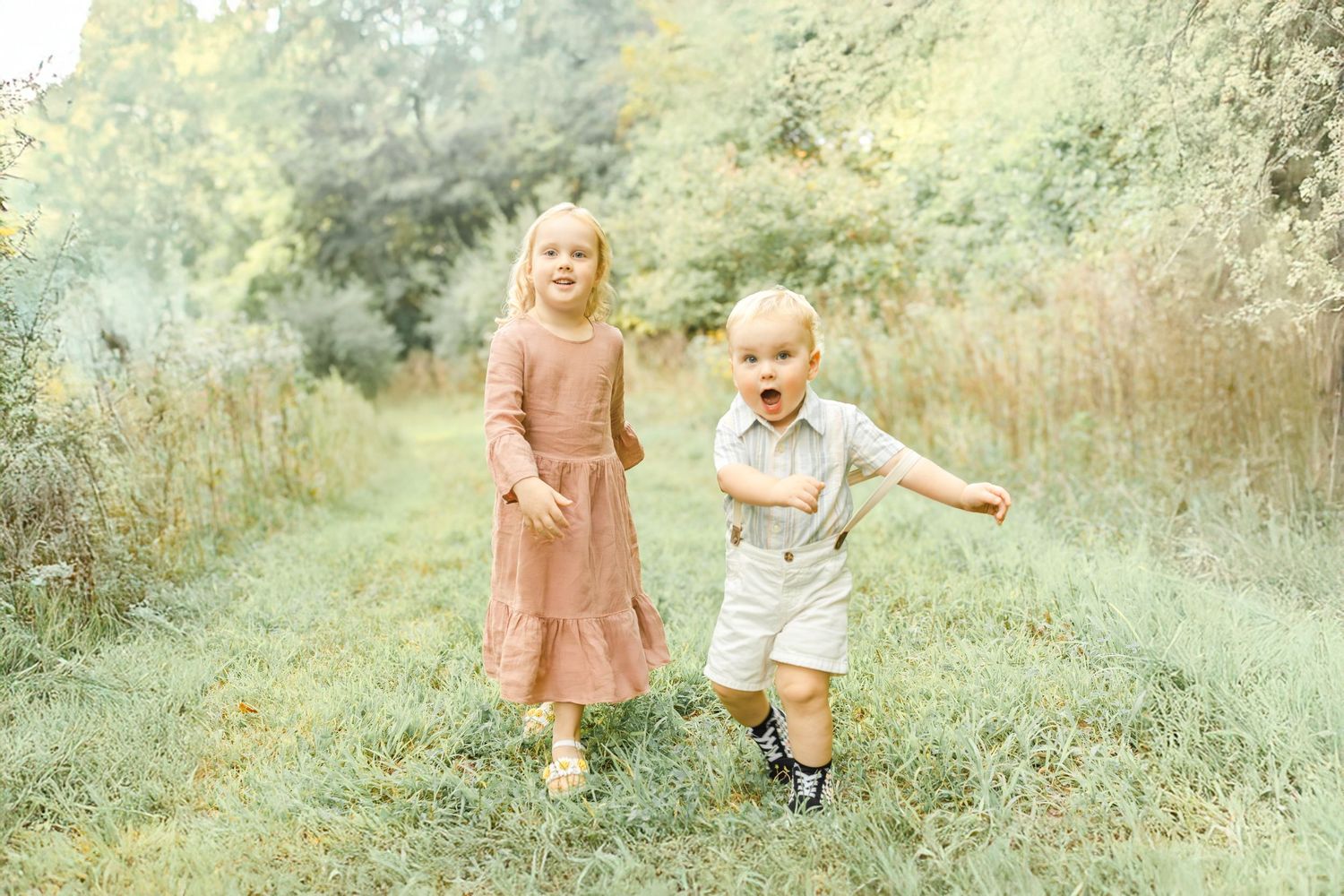Two young children walking together through a grassy path during an outdoor family photo session.
