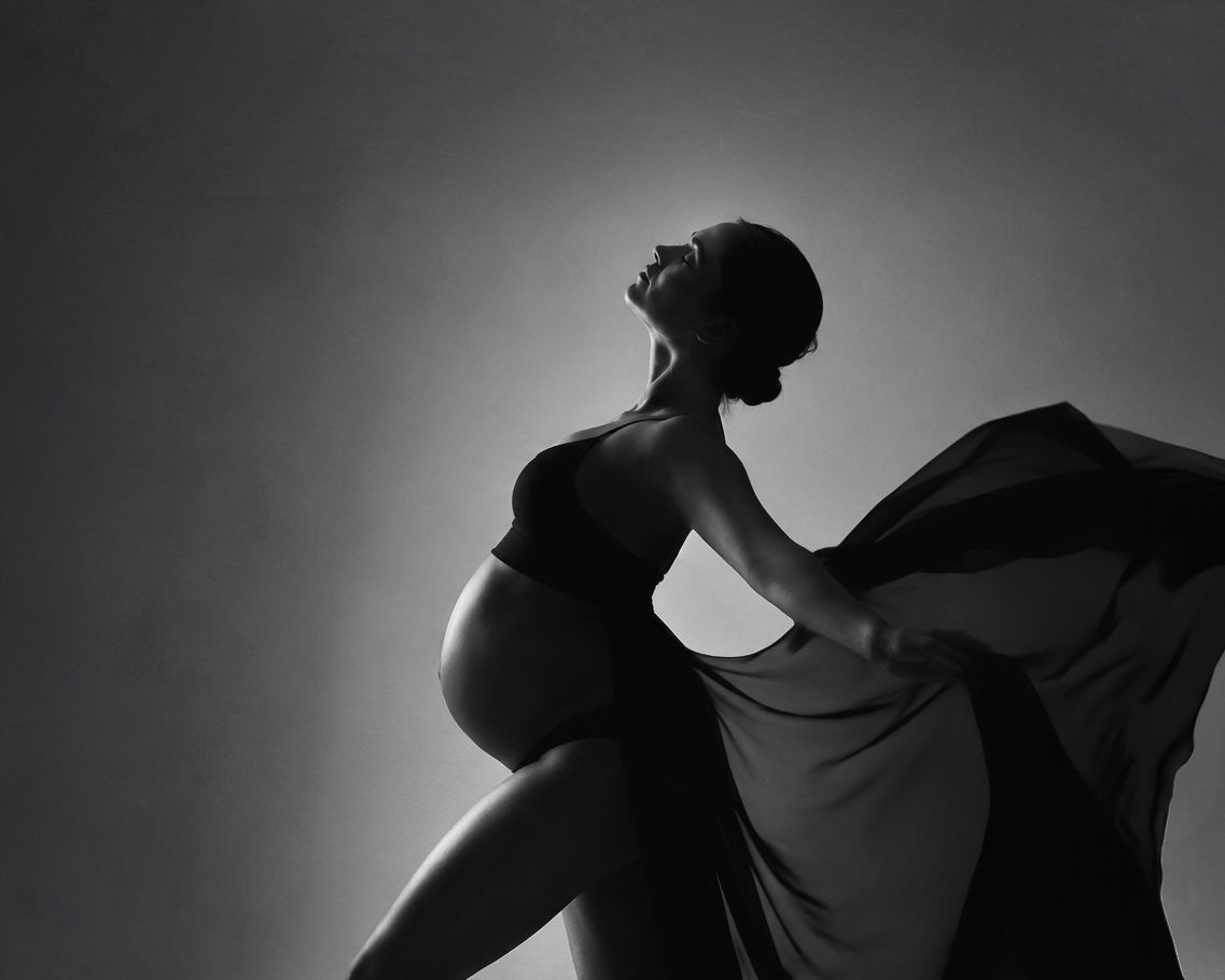 Black and white silhouette of an expectant mother holding flowing fabric during a fine art maternity photography session.