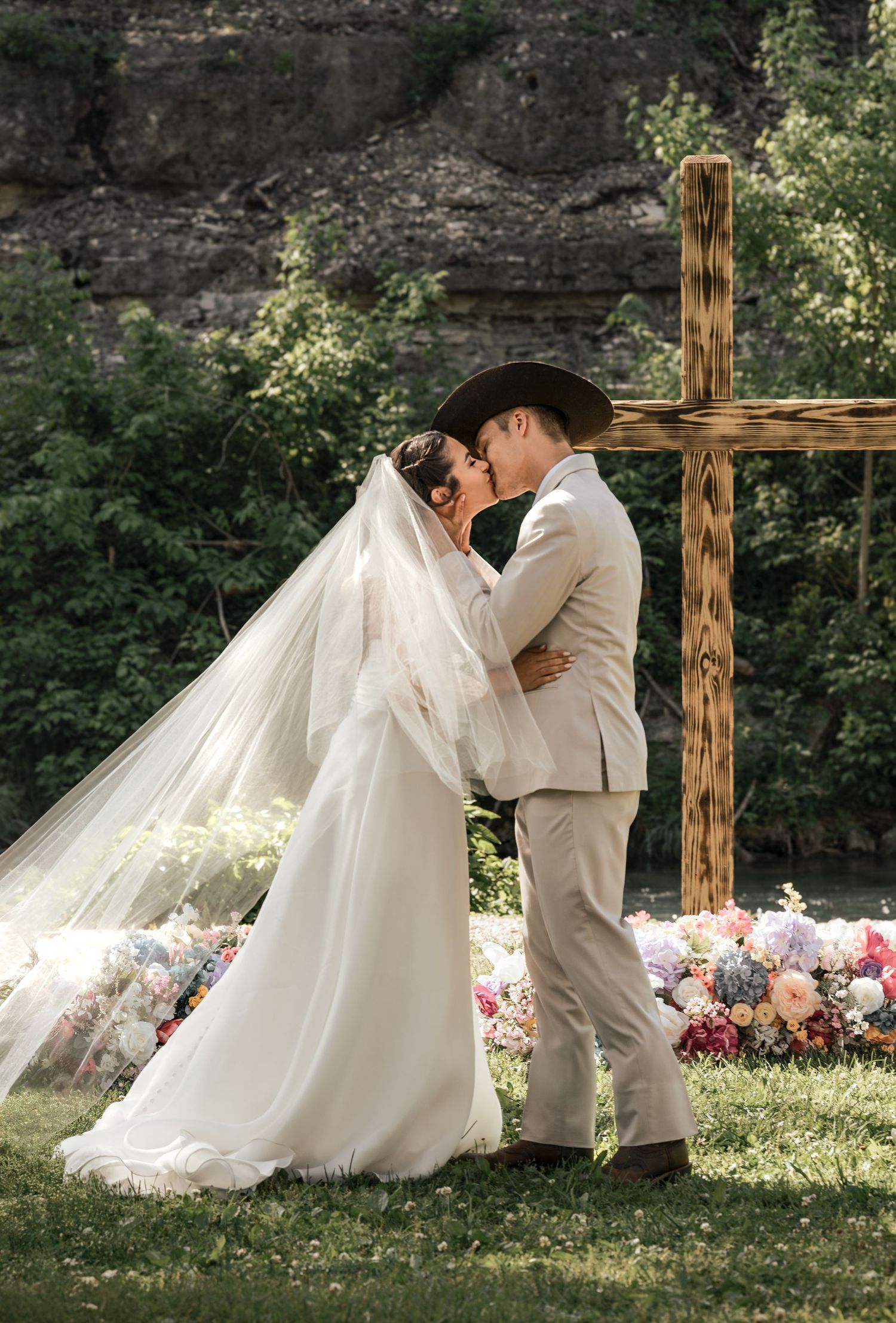Bride and groom kissing beneath wooden cross during outdoor wedding ceremony at Roaring River State Park