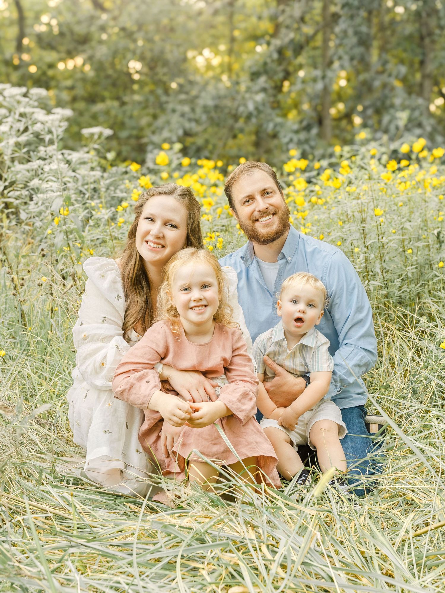 A family of four sitting together in a grassy field during a relaxed outdoor photo session in Kansas City.